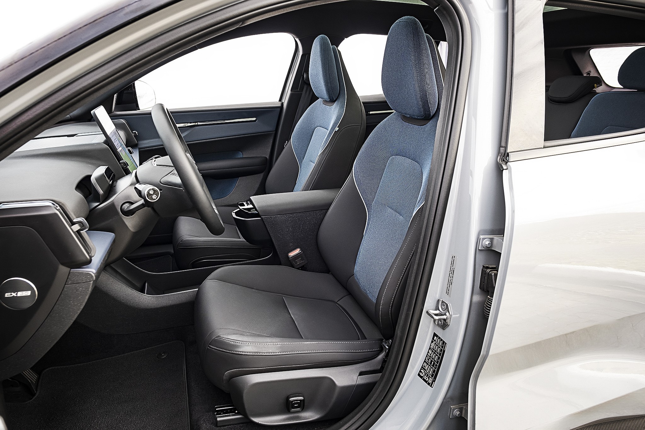 Interior de um carro com a porta do motorista aberta, mostrando os bancos dianteiros em couro preto e tecido azul, volante e painel escuros com detalhes prateados e uma tela vertical no centro