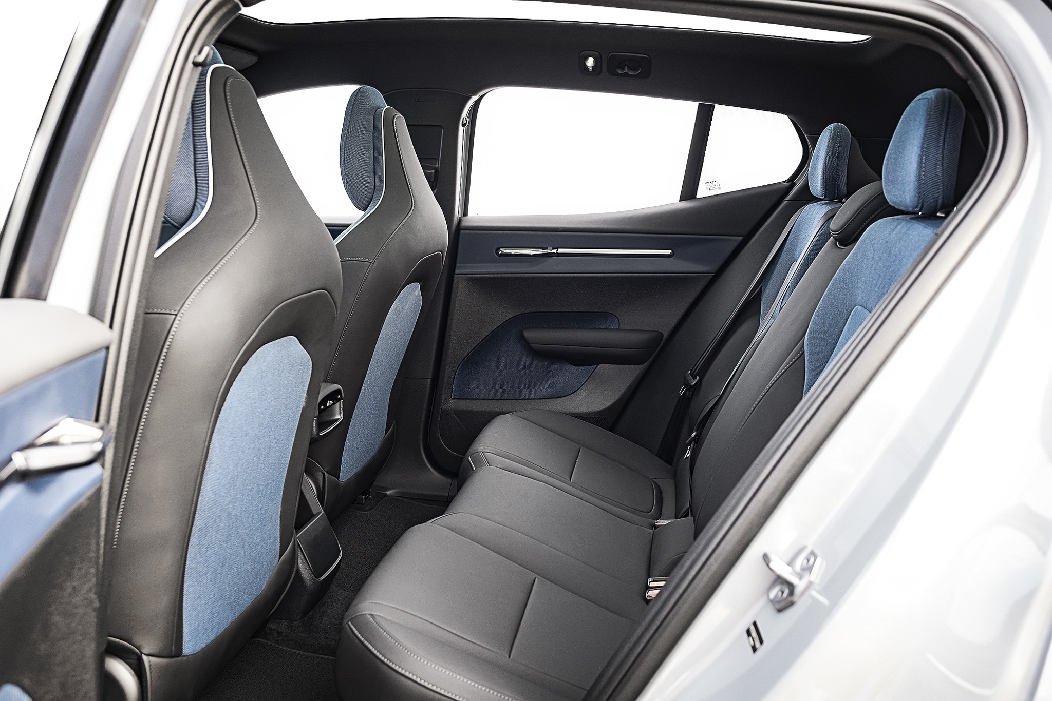 Interior de um carro com bancos de couro preto e detalhes em tecido azul claro. Os bancos dianteiros t&ecirc;m encostos altos e os traseiros s&atilde;o um banco corrido para tr&ecirc;s pessoas. As portas t&ecirc;m acabamento em azul escuro e detalhes cromados. As janelas est&atilde;o abertas, mostrando um fundo branco