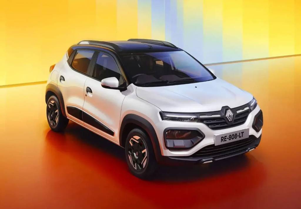Carro Renault Kwid branco com teto preto, visto de frente e ligeiramente de cima, em um est&uacute;dio com fundo e ch&atilde;o em tons de laranja, amarelo e vermelho