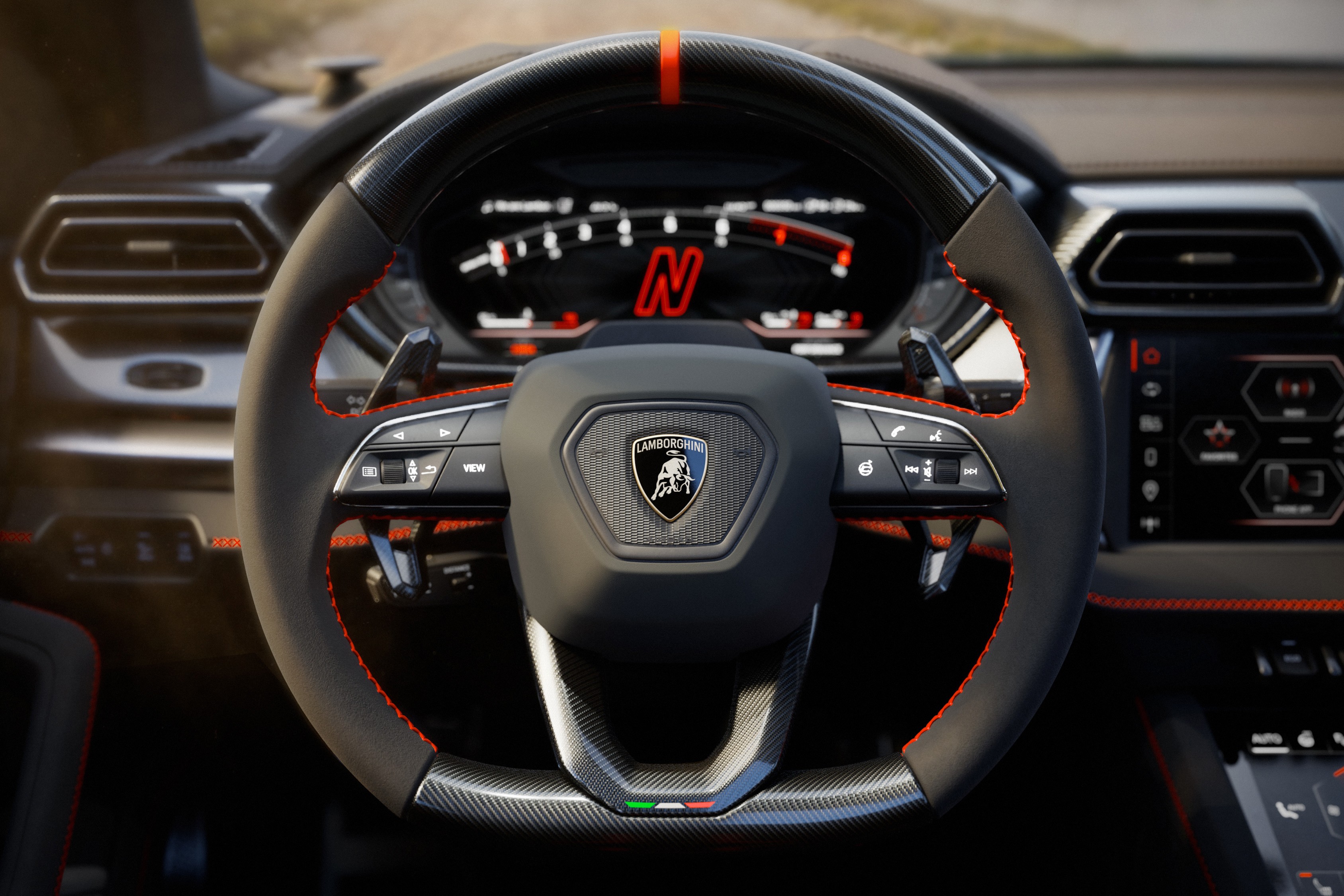 Volante de carro esportivo Lamborghini Urus em couro preto com costura vermelha, detalhes em fibra de carbono e o emblema da marca ao centro. O painel digital exibe a letra N em vermelho, indicando o modo de condu&ccedil;&atilde;o.