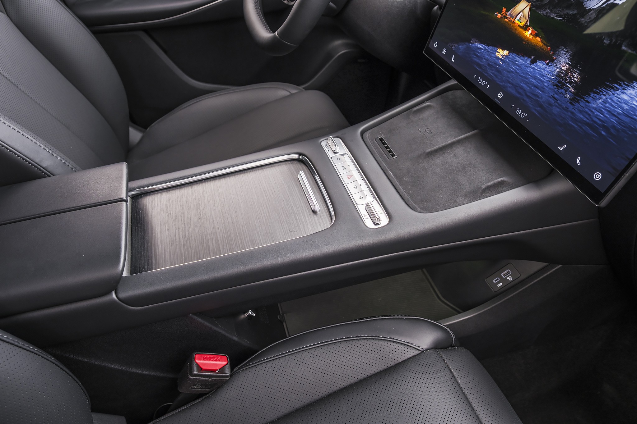 Interior de carro moderno com console central em preto e cinza escovado, bancos de couro perfurado e tela multim&iacute;dia exibindo uma paisagem noturna com barco iluminado