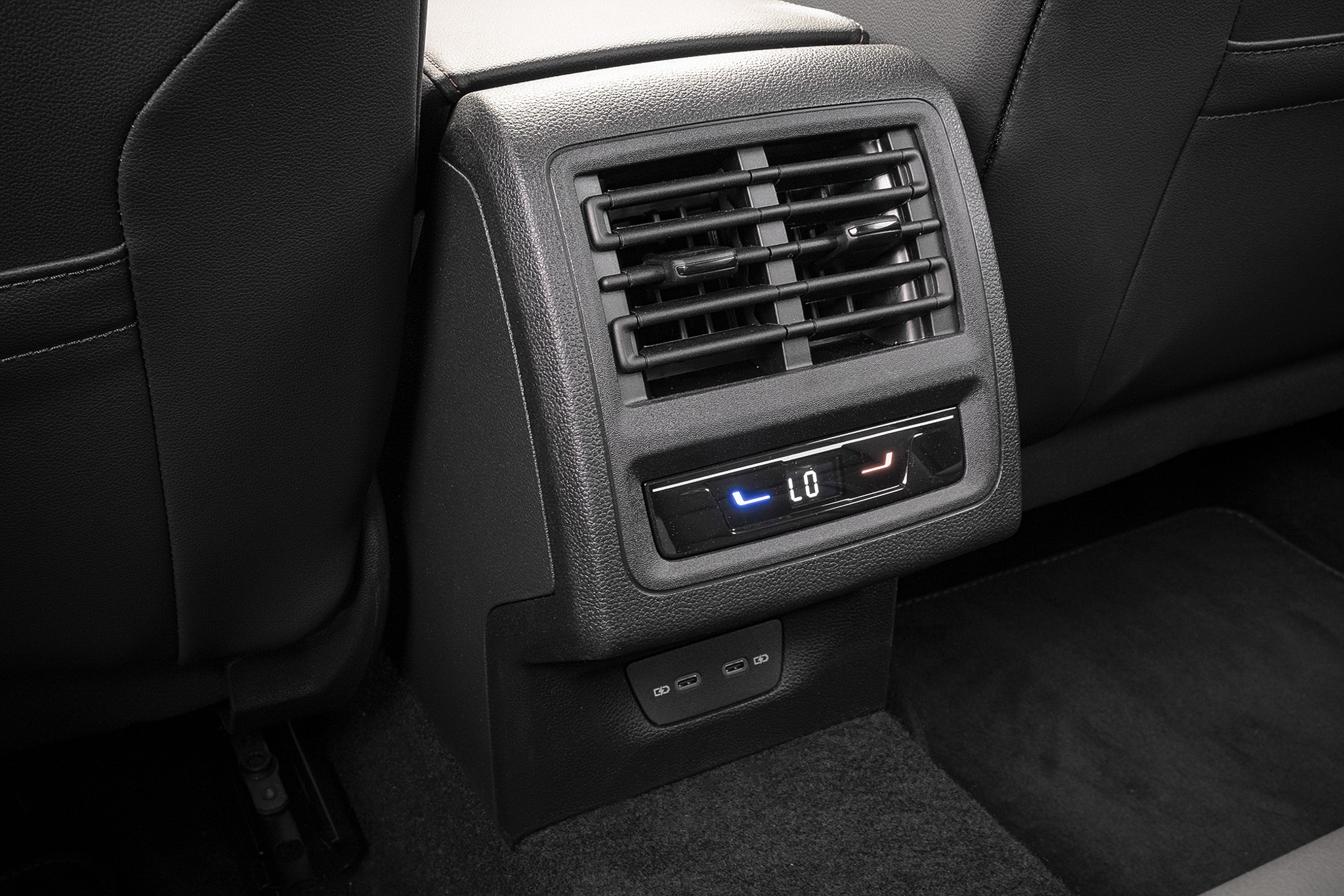 Painel traseiro de um carro com sa&iacute;das de ar, controle digital de temperatura LO e duas portas USB-C abaixo, entre os bancos dianteiros