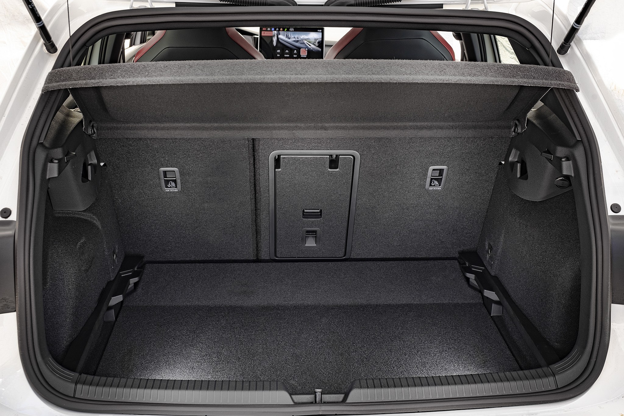 Porta-malas de um carro hatch, forrado com carpete cinza escuro, com o tamp&atilde;o do bagageiro levantado. Ao fundo, os bancos traseiros rebatidos e uma tela de multim&iacute;dia vis&iacute;vel