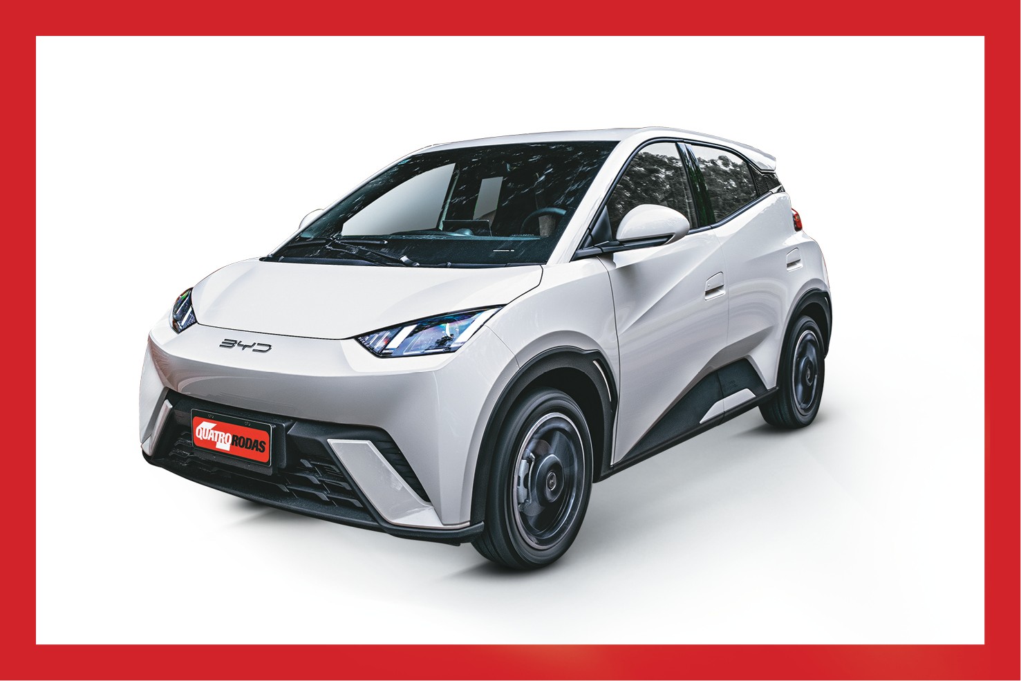 Carro el&eacute;trico BYD Dolphin branco, visto de frente e lateralmente, com o logotipo da marca na grade e a placa Quatro Rodas no para-choque, em fundo branco com borda vermelha