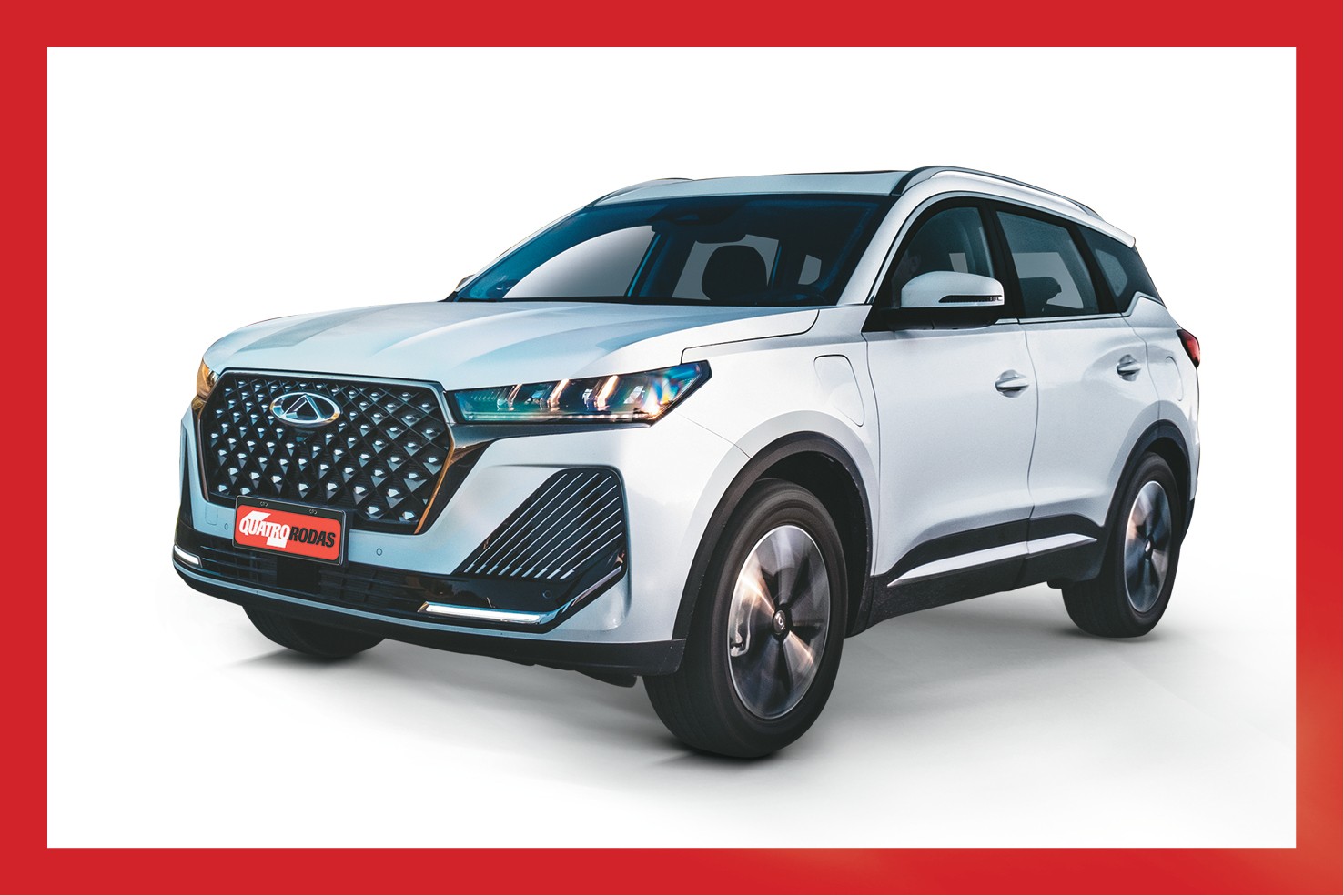 SUV branco da marca Chery, modelo Tiggo 8 Pro, visto de frente e levemente de lado, com a grade frontal preta e cromada, far&oacute;is acesos e placa vermelha QUATRO RODAS
