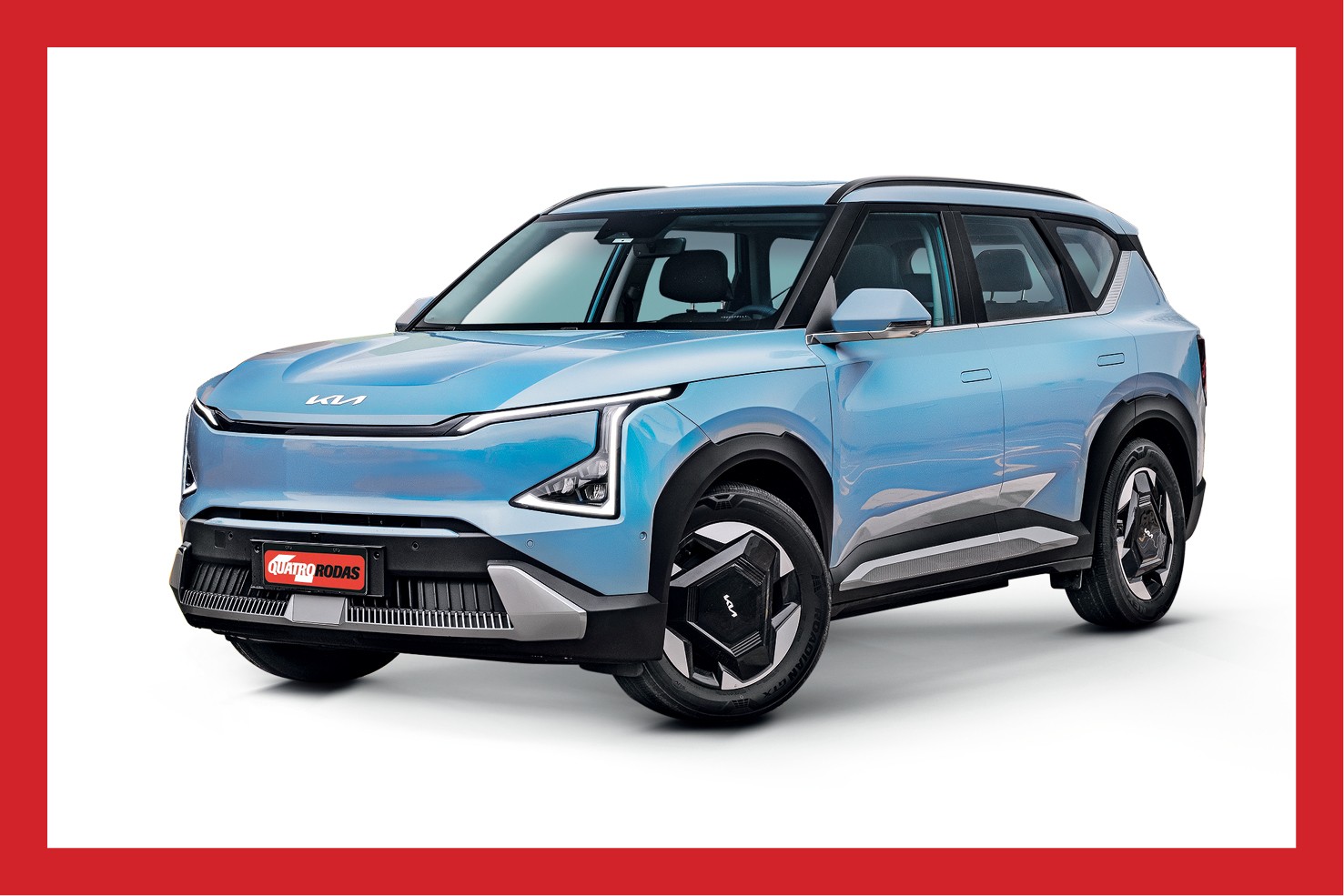 SUV Kia EV5 azul claro, com design futurista e linhas retas, em fundo branco. O carro el&eacute;trico tem far&oacute;is em LED, rodas pretas com detalhes geom&eacute;tricos e o logotipo da revista Quatro Rodas na grade frontal
