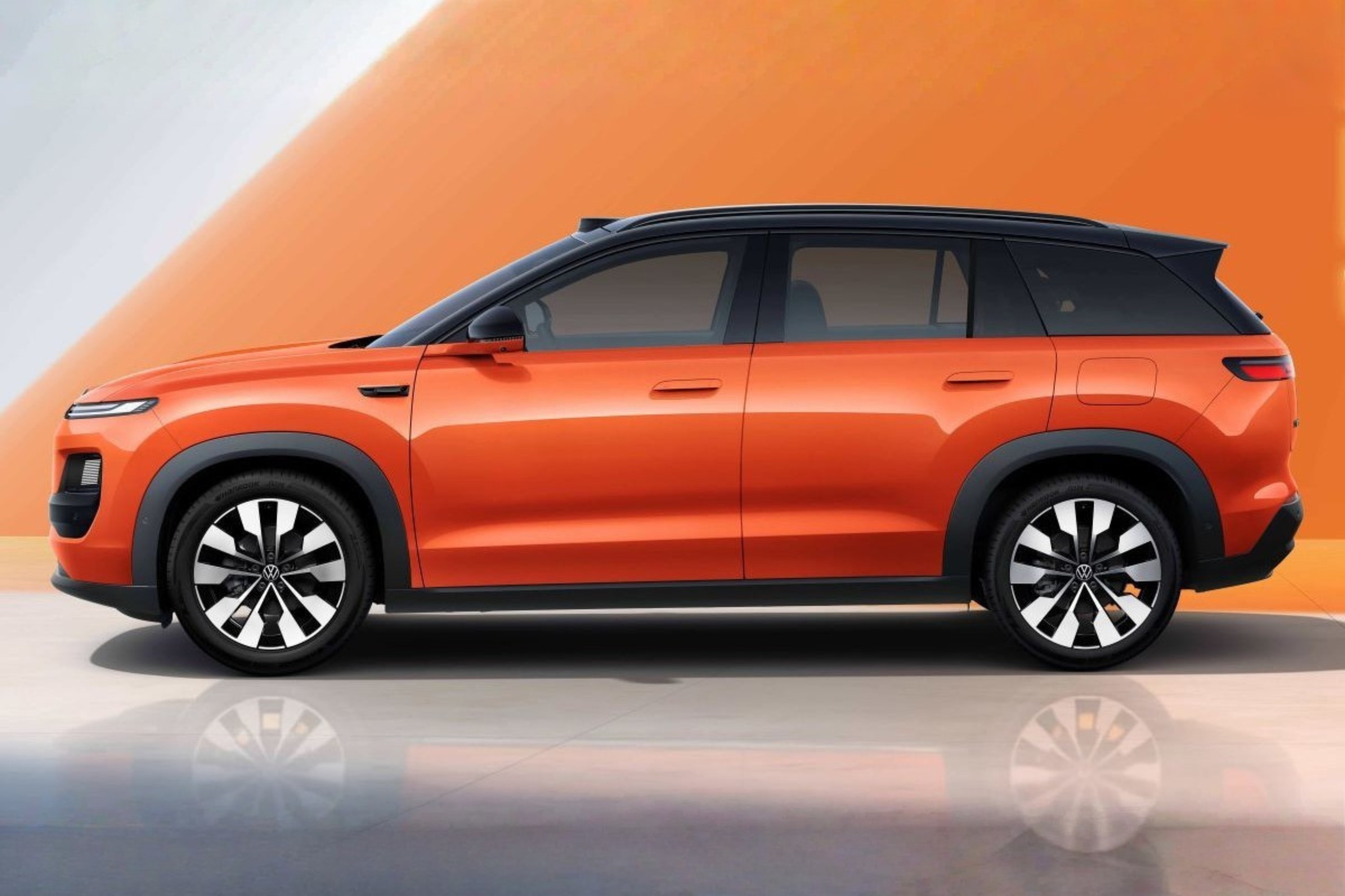 SUV laranja com teto preto, visto de perfil, parado sobre uma superf&iacute;cie cinza que reflete suas rodas. O fundo &eacute; laranja com uma faixa diagonal branca