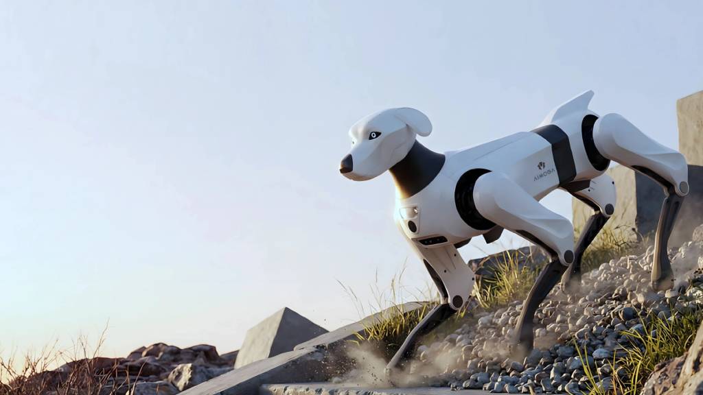 Cachorro rob&oacute;tico branco e preto, com o nome AIBOBA na lateral, correndo sobre pedras e terra, levantando poeira, em um cen&aacute;rio &aacute;rido sob c&eacute;u claro