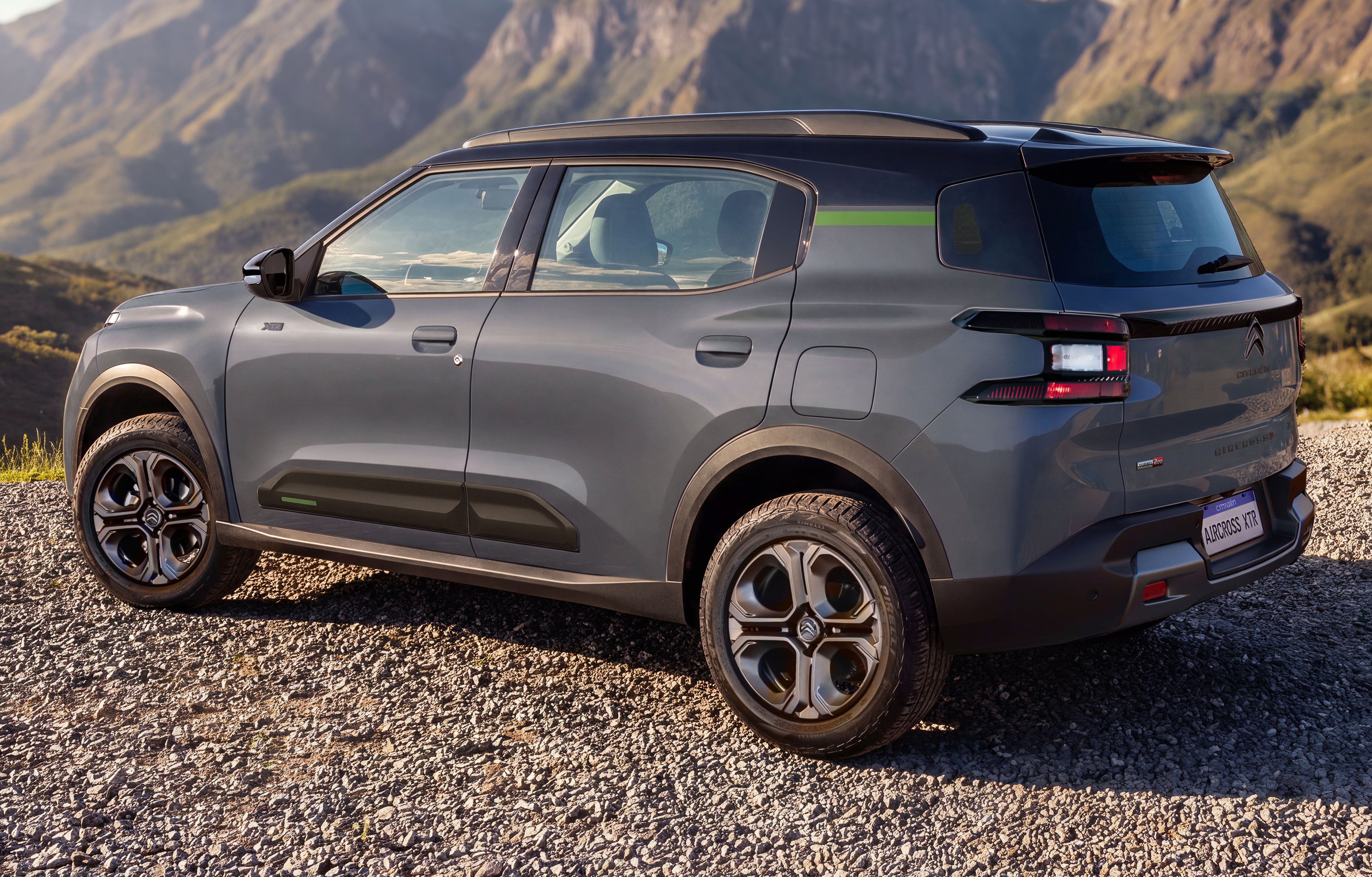SUV Citro&euml;n C3 Aircross cinza escuro, com teto preto e faixa verde na lateral, estacionado em estrada de cascalho com montanhas ao fundo