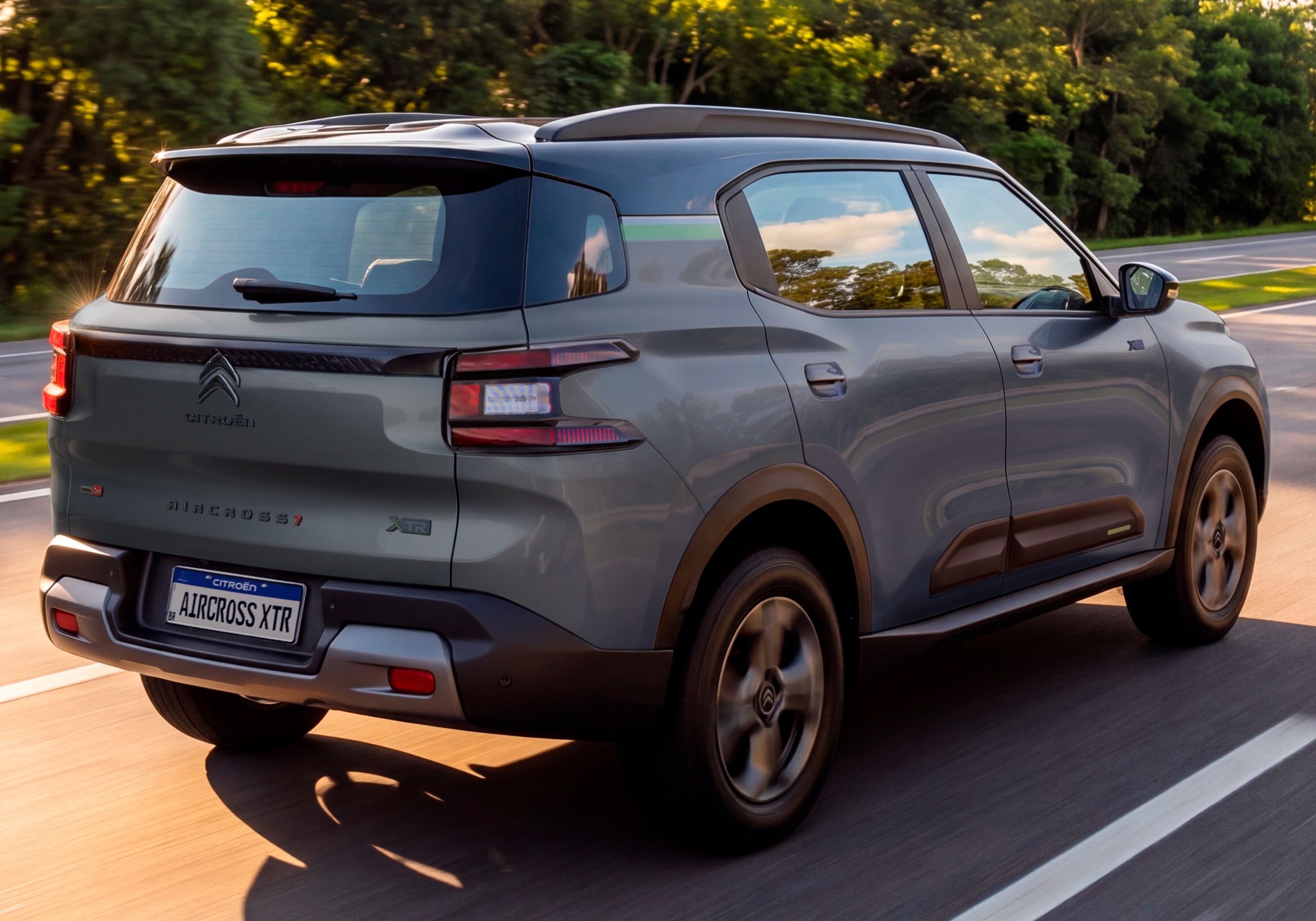 SUV Citro&euml;n Aircross XTR cinza escuro, visto de traseira e lateral, em movimento numa estrada asfaltada com &aacute;rvores ao fundo