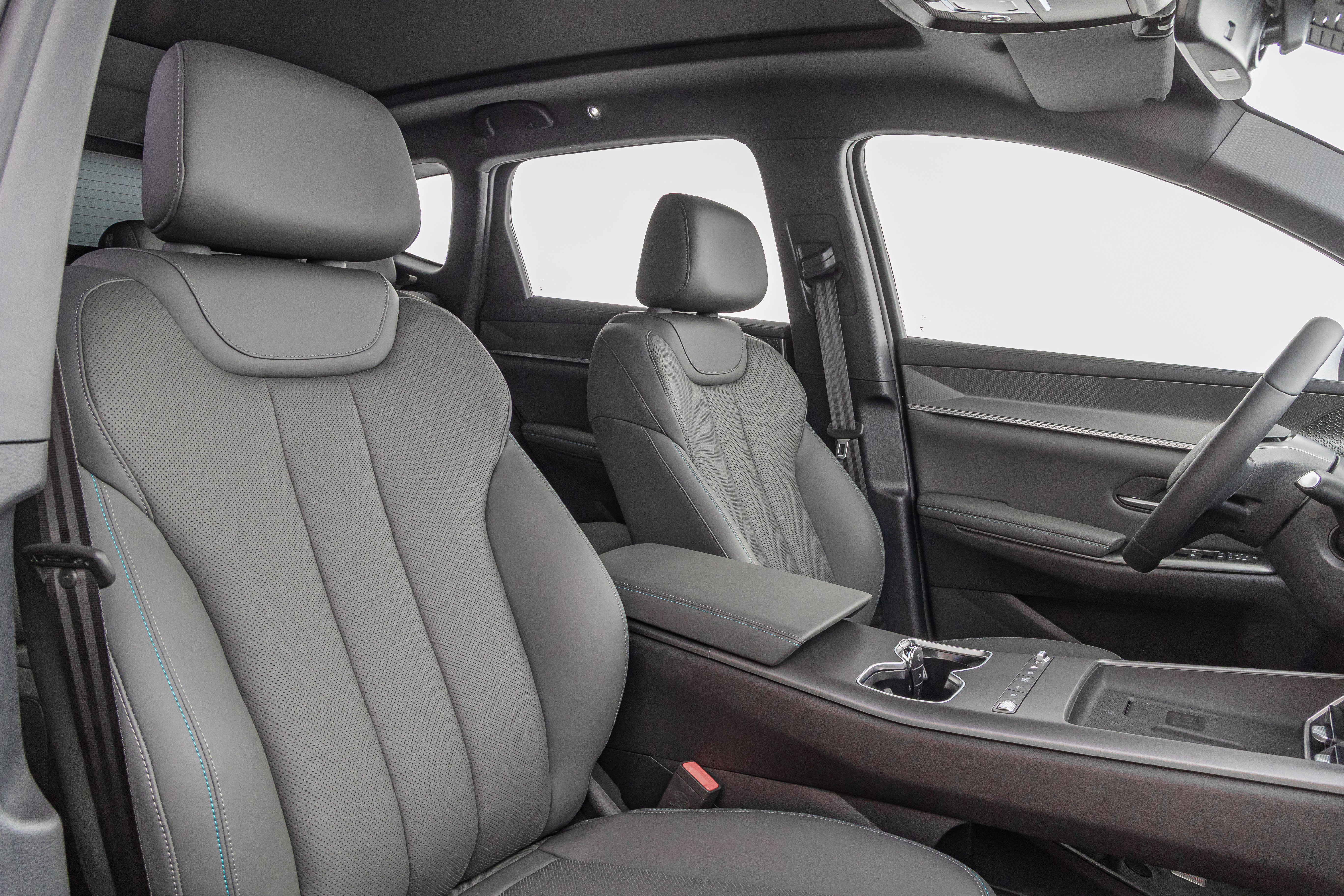 Interior de um carro moderno com bancos de couro cinza perfurado e costura azul. O banco do motorista est&aacute; em primeiro plano, com o banco do passageiro e o console central vis&iacute;veis ao fundo. O volante e parte do painel tamb&eacute;m aparecem &agrave; direita