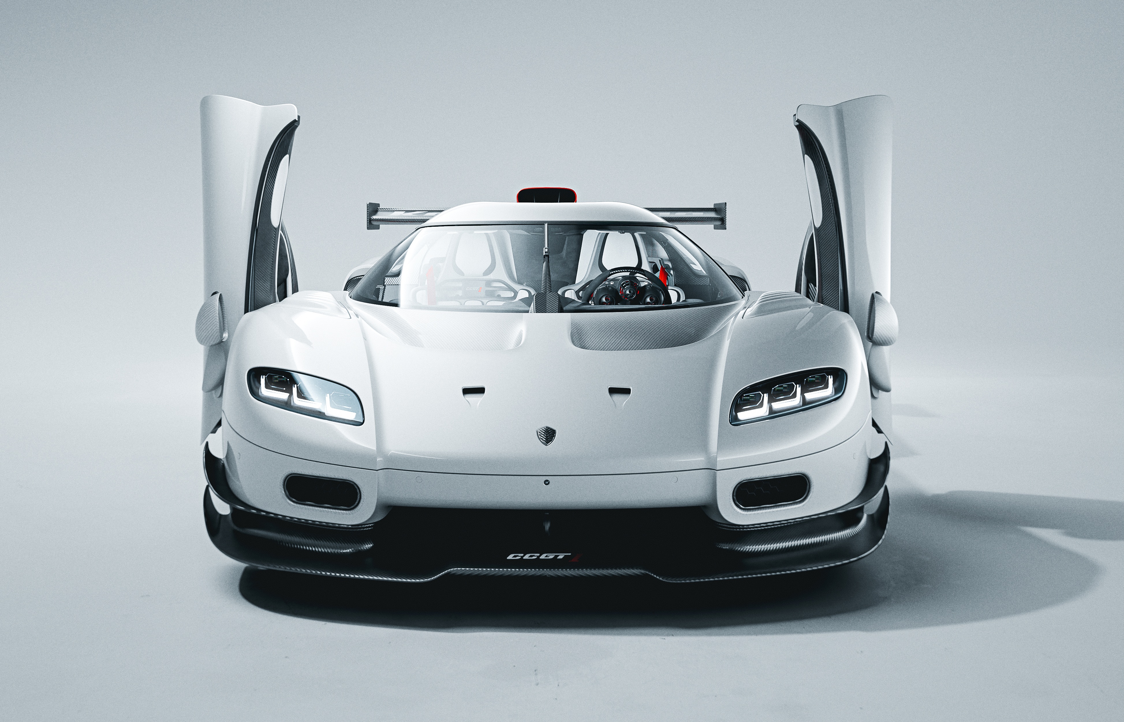 Carro esportivo branco Koenigsegg CCGT, com portas abertas para cima, far&oacute;is acesos e aerof&oacute;lio traseiro, em est&uacute;dio claro