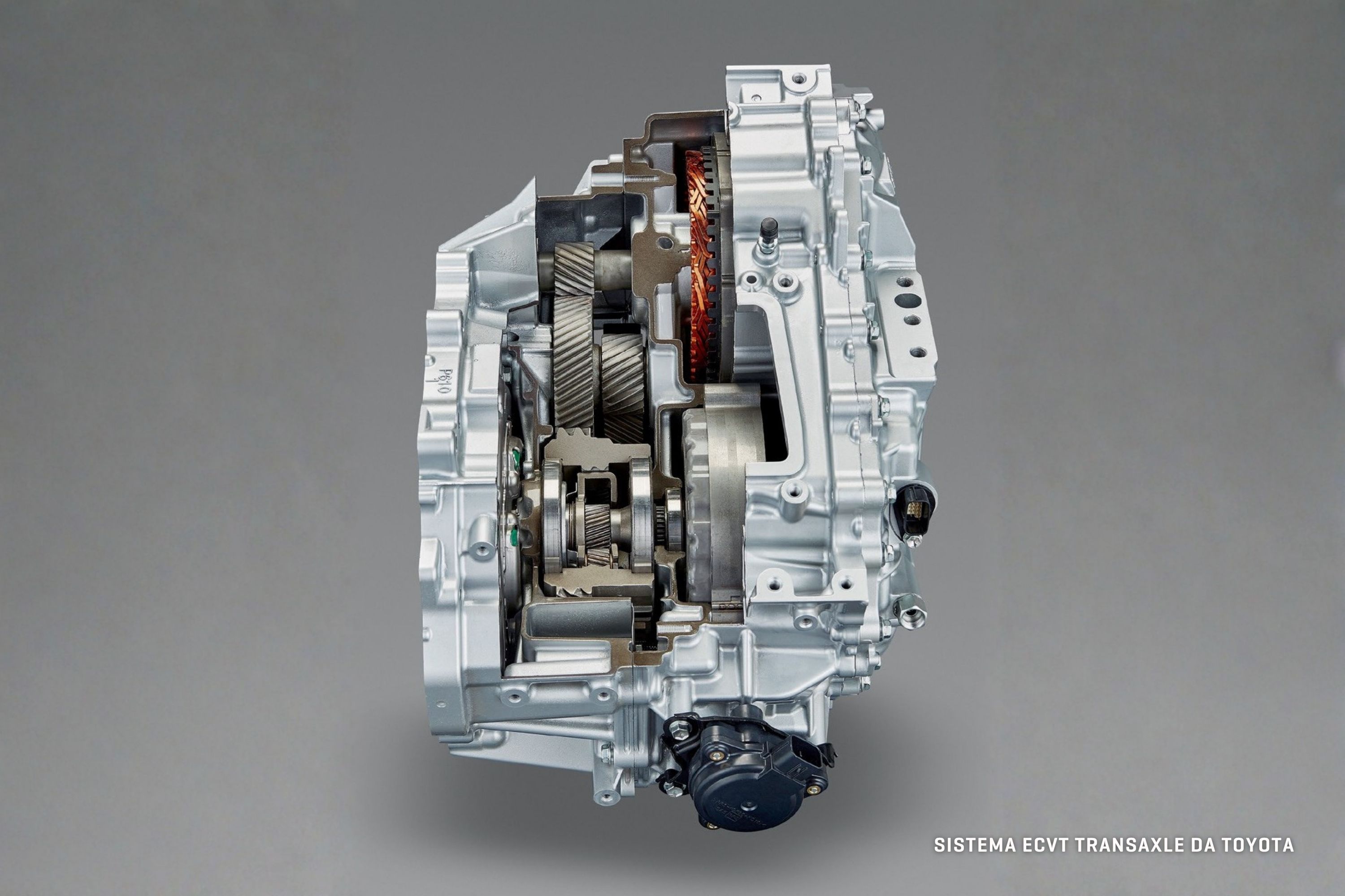 Transmiss&atilde;o eCVT Transaxle da Toyota, com carca&ccedil;a prateada cortada ao meio, revelando engrenagens, bobinas de cobre e componentes internos em tons de cinza e preto, sobre fundo cinza liso