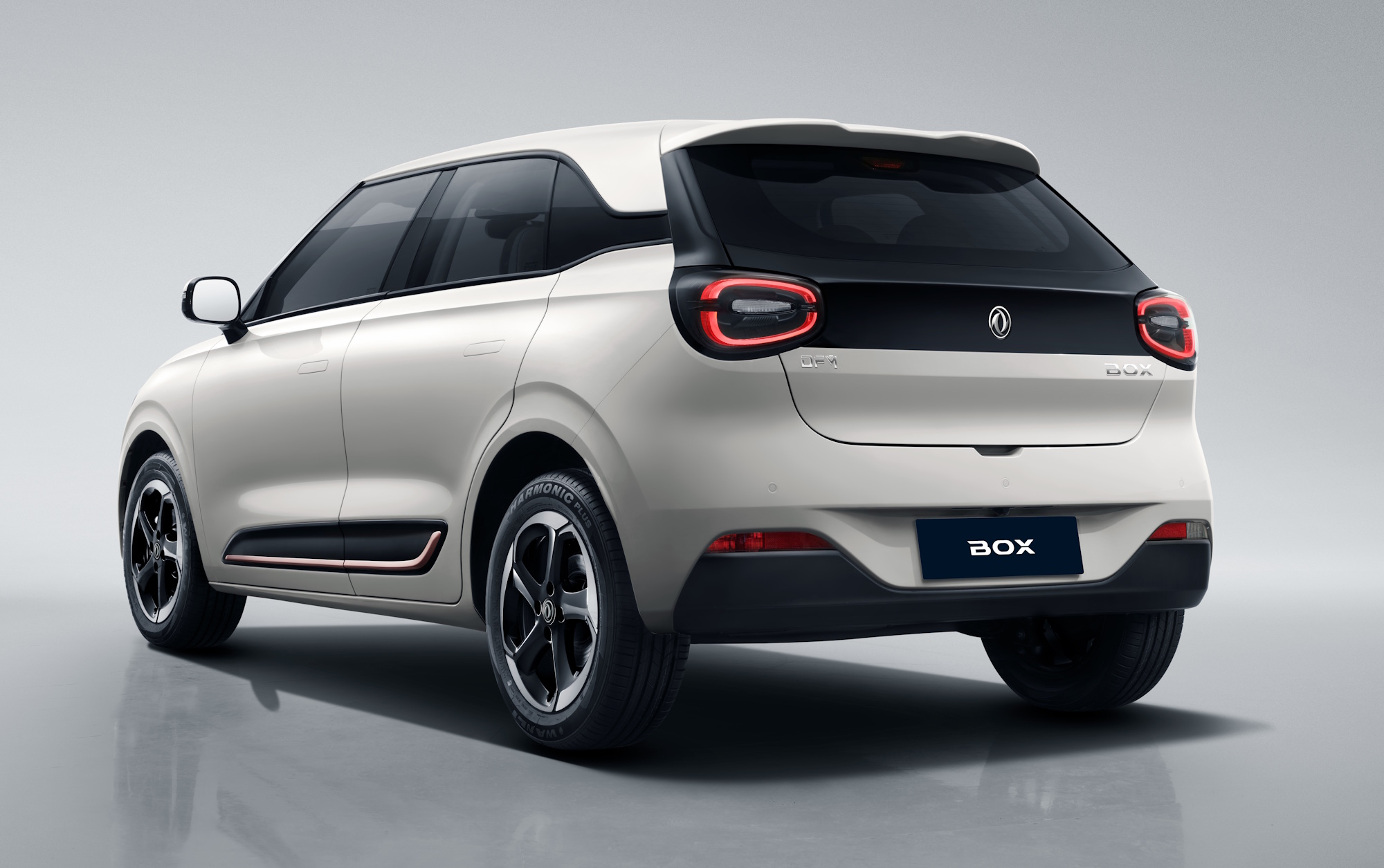 Carro el&eacute;trico branco, modelo SUV compacto, visto de traseira e lateral direita, com detalhes em preto na tampa do porta-malas e nas rodas. As lanternas traseiras s&atilde;o em formato de C invertido e a placa exibe BOX em branco sobre fundo azul escuro. O ve&iacute;culo est&aacute; em um est&uacute;dio com fundo cinza claro e reflexo no ch&atilde;o