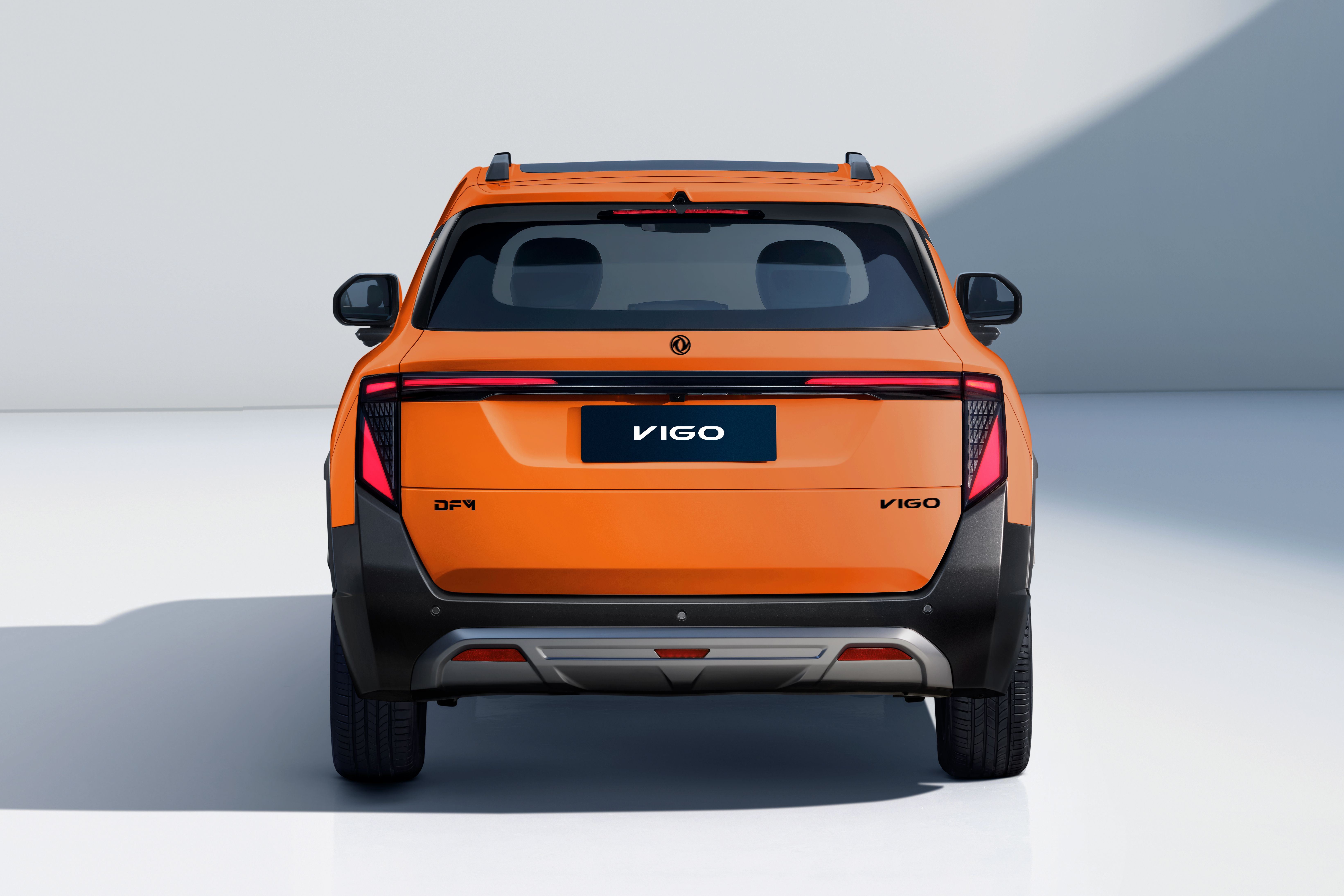 Traseira de um carro laranja VIGO, com detalhes em preto fosco e um para-choque prateado. As lanternas verticais t&ecirc;m luzes vermelhas acesas, e o nome VIGO aparece na placa e no canto inferior direito da tampa do porta-malas. O ve&iacute;culo est&aacute; em um est&uacute;dio branco com sombras suaves