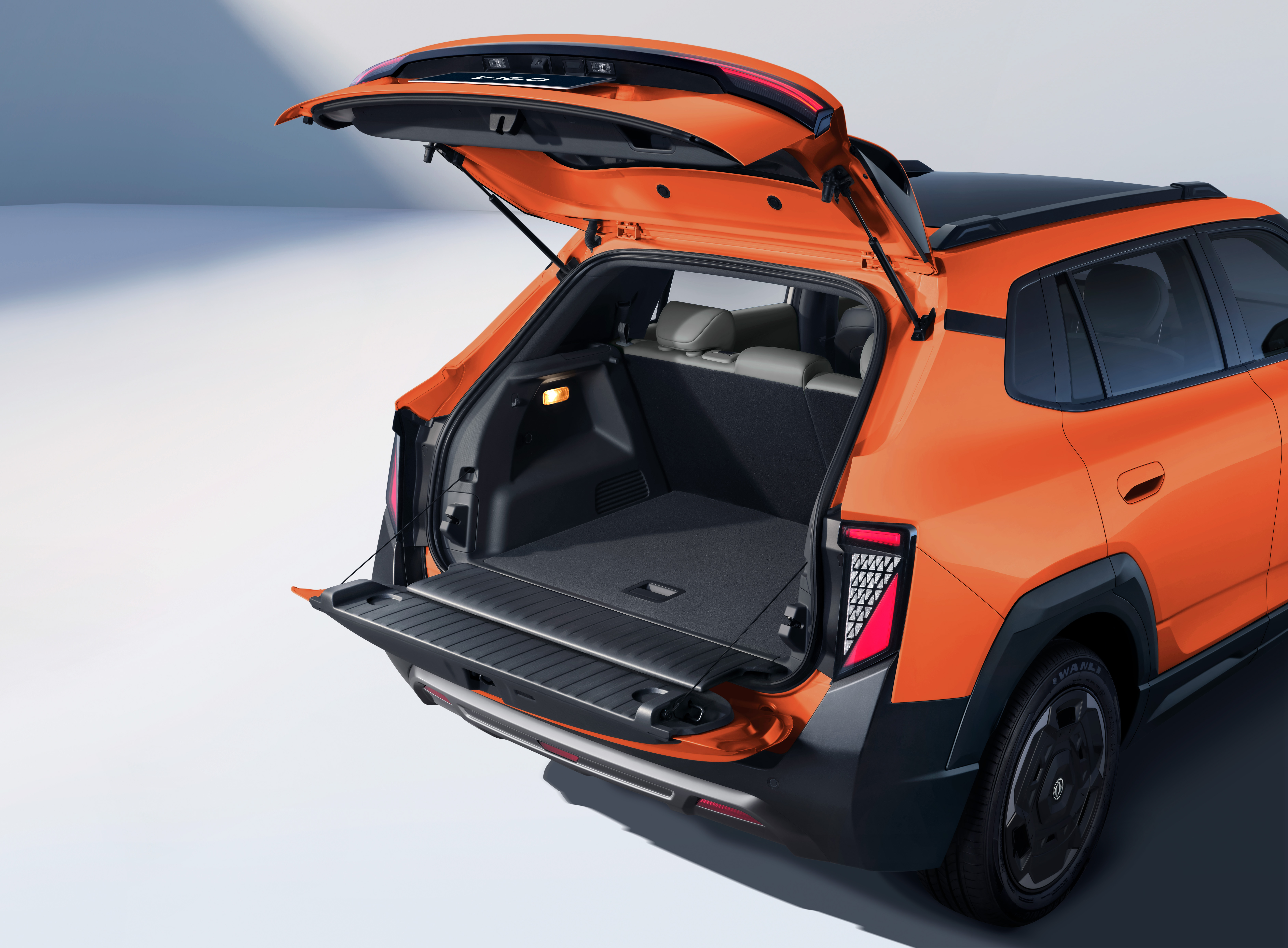 Traseira de um SUV laranja com a tampa do porta-malas aberta, revelando um amplo espa&ccedil;o interno e uma prateleira retr&aacute;til. As lanternas traseiras t&ecirc;m design moderno e o para-choque &eacute; preto com detalhes prateados. O ve&iacute;culo est&aacute; em um est&uacute;dio com fundo claro