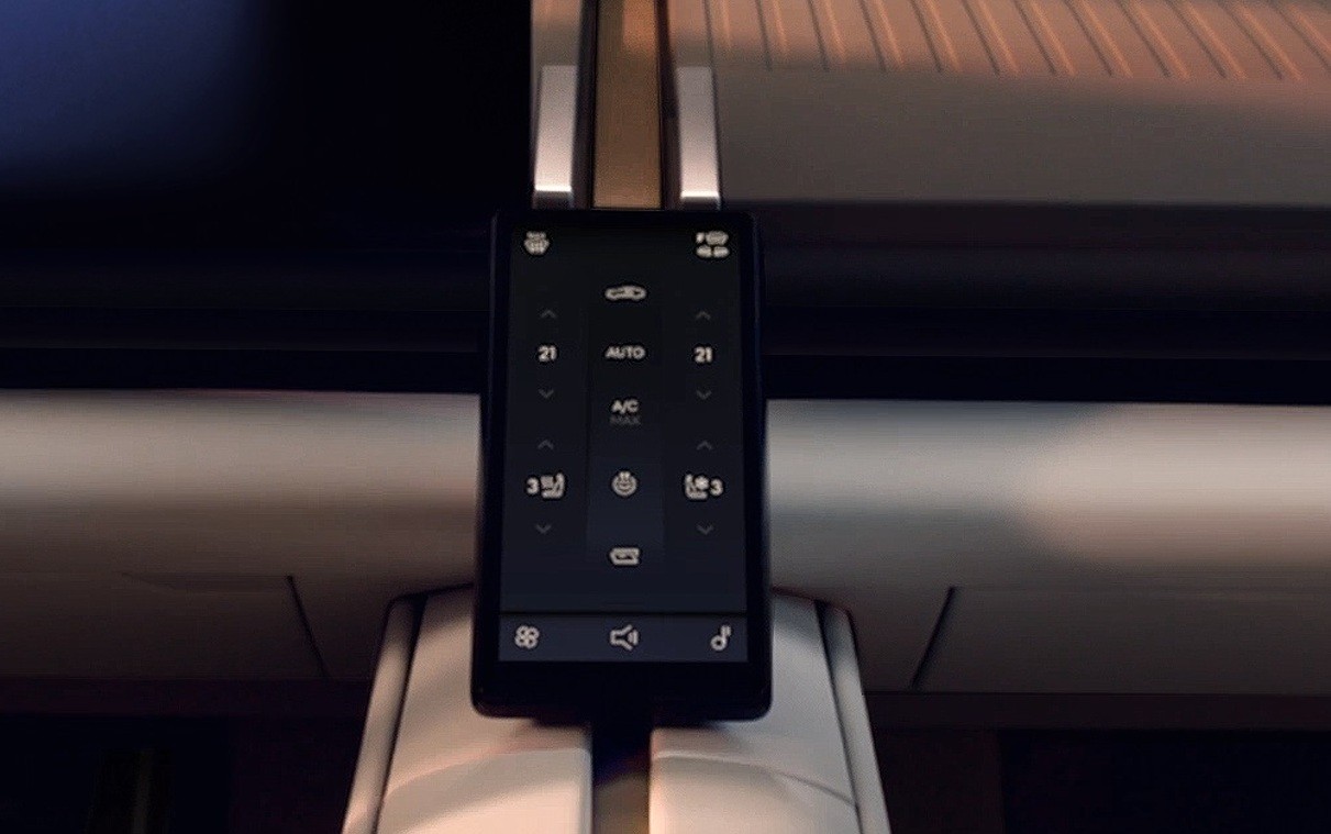 Tela de controle digital de um carro, exibindo configura&ccedil;&otilde;es de ar-condicionado com temperatura 21 graus, modo autom&aacute;tico e bot&otilde;es para ventila&ccedil;&atilde;o e outras fun&ccedil;&otilde;es. Na parte inferior, &iacute;cones de aplicativos e m&uacute;sica. A tela est&aacute; encaixada em um suporte no painel do ve&iacute;culo, com detalhes em tons escuros e claros