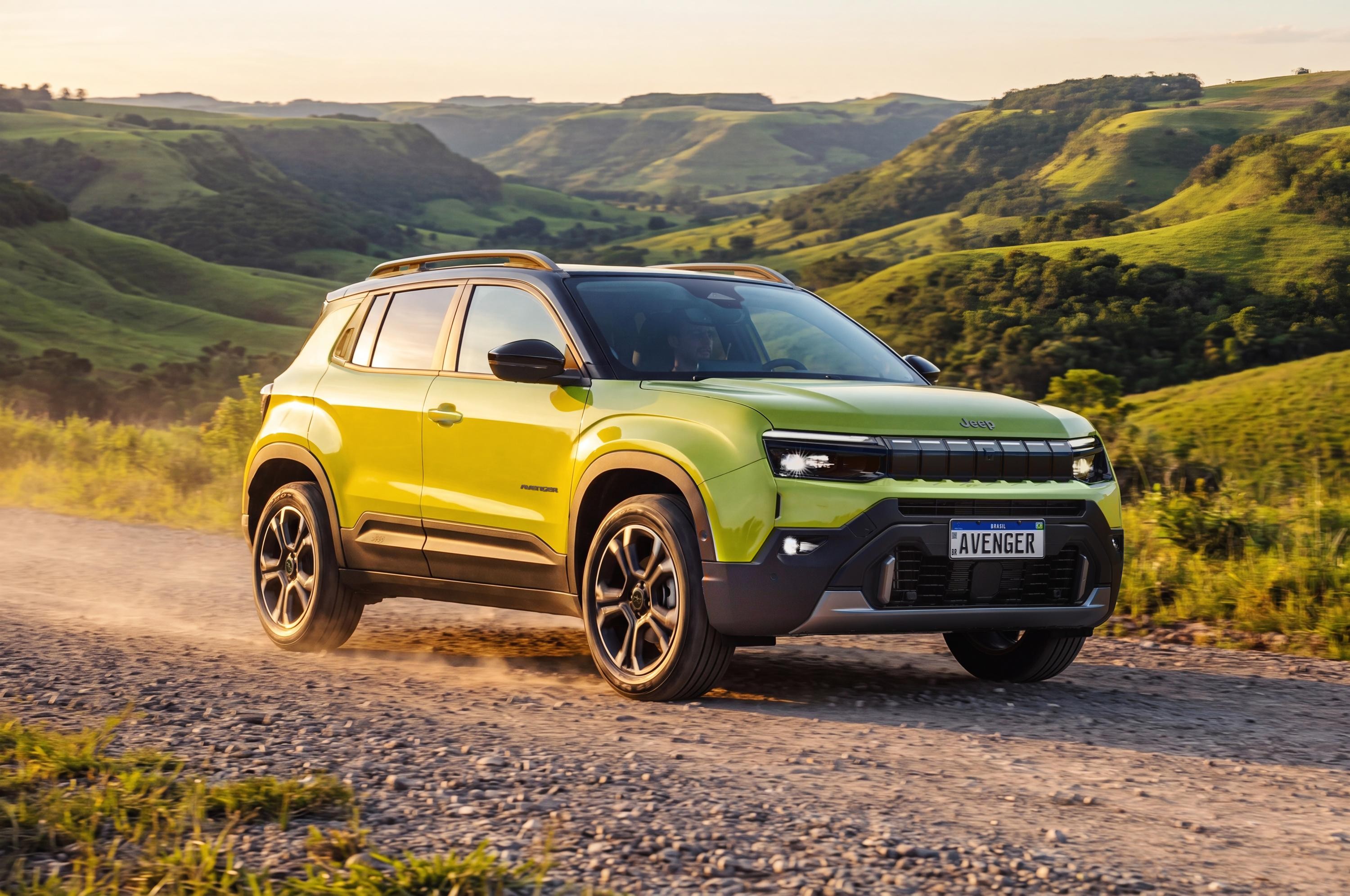 SUV Jeep Avenger amarelo-lim&atilde;o com teto preto e rack de teto, em estrada de terra com poeira, contra um cen&aacute;rio de colinas verdes e c&eacute;u claro ao p&ocirc;r do sol