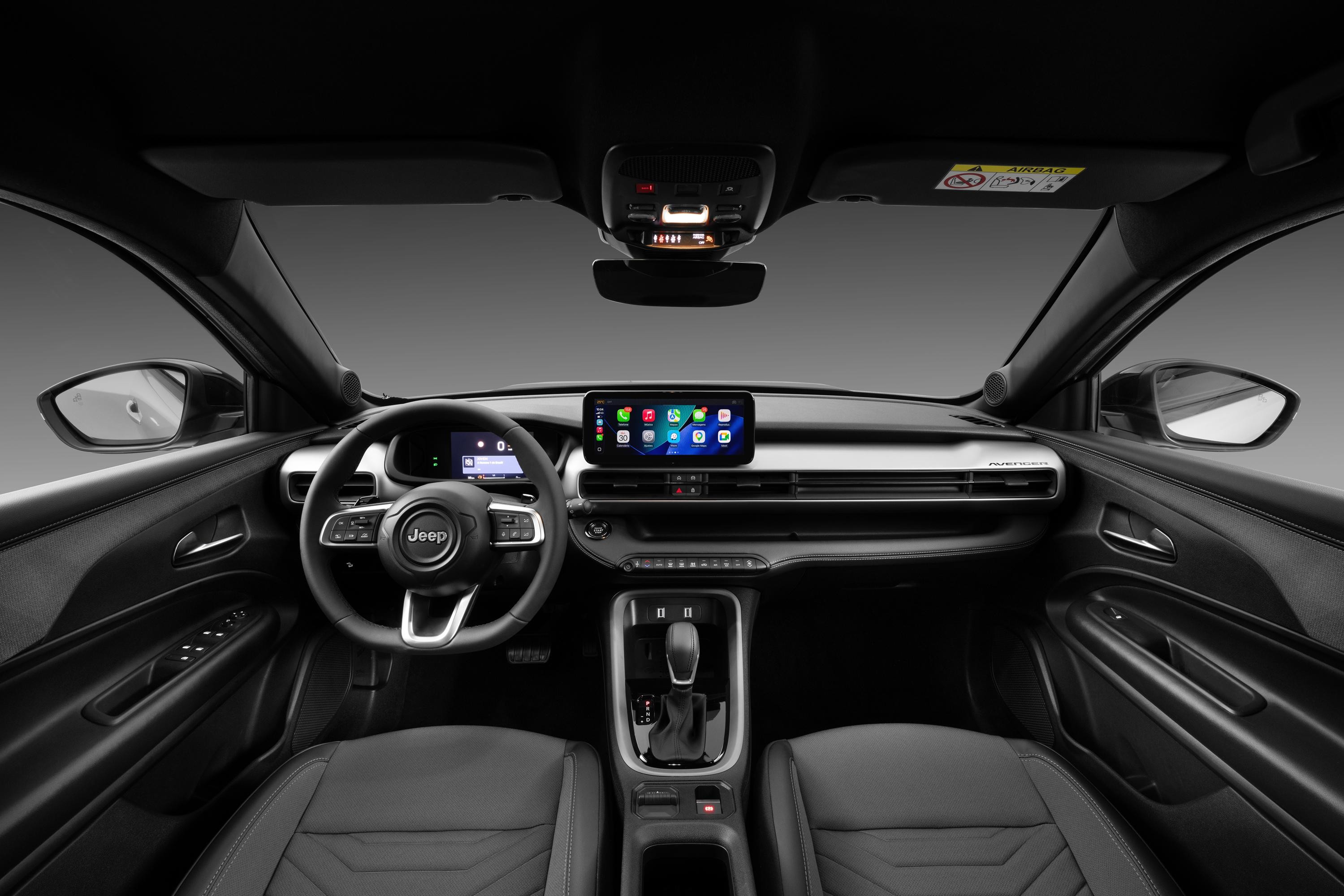 Interior de um carro Jeep com painel e bancos pretos, volante multifuncional com logo Jeep, tela multim&iacute;dia central exibindo &iacute;cones de aplicativos e console com c&acirc;mbio autom&aacute;tico