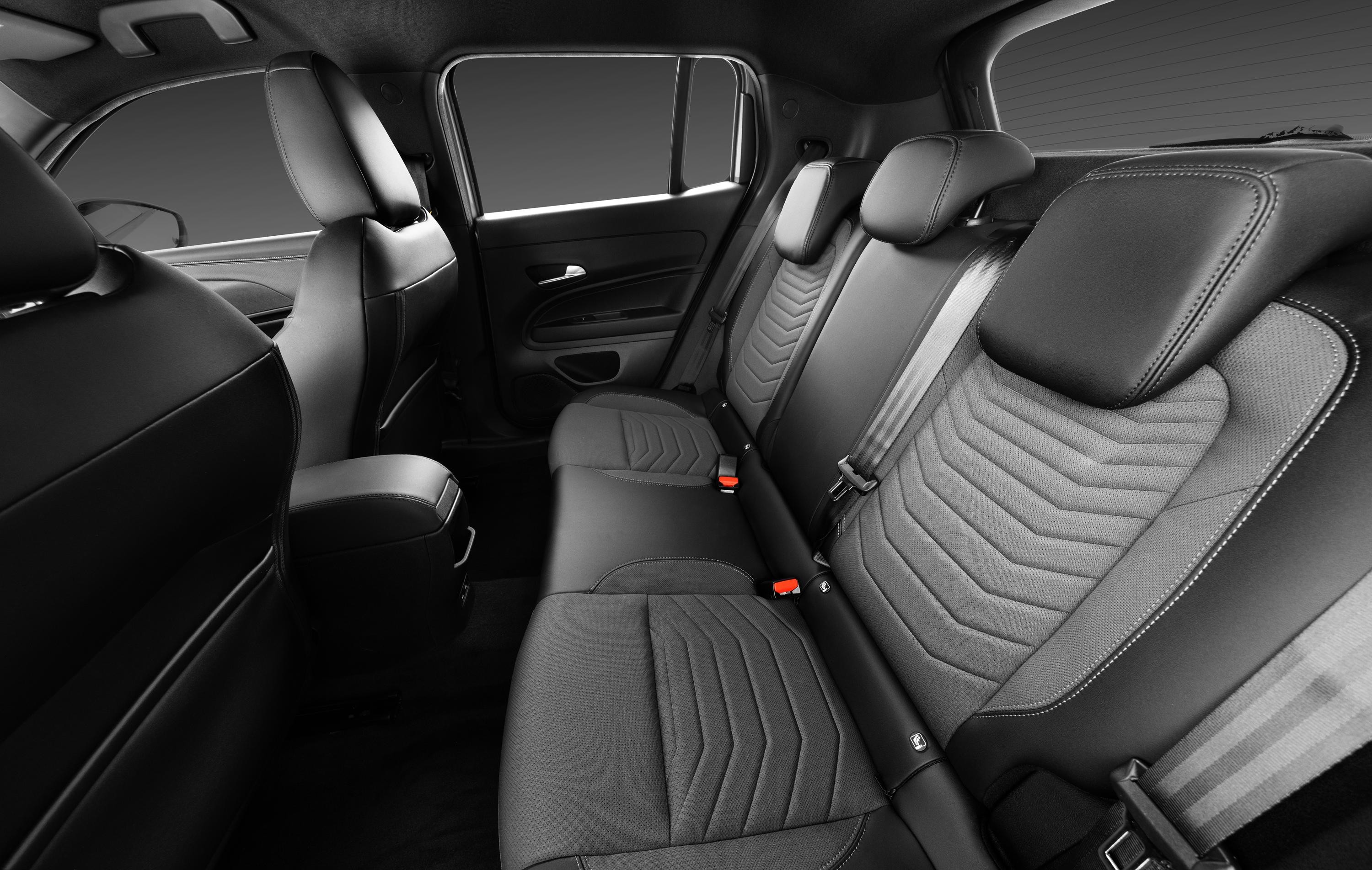 Interior de um carro com bancos traseiros em couro preto e tecido cinza escuro, com costuras brancas e padr&atilde;o geom&eacute;trico em zigue-zague. Os cintos de seguran&ccedil;a est&atilde;o vis&iacute;veis, e o banco do passageiro dianteiro &eacute; parcialmente vis&iacute;vel &agrave; esquerda