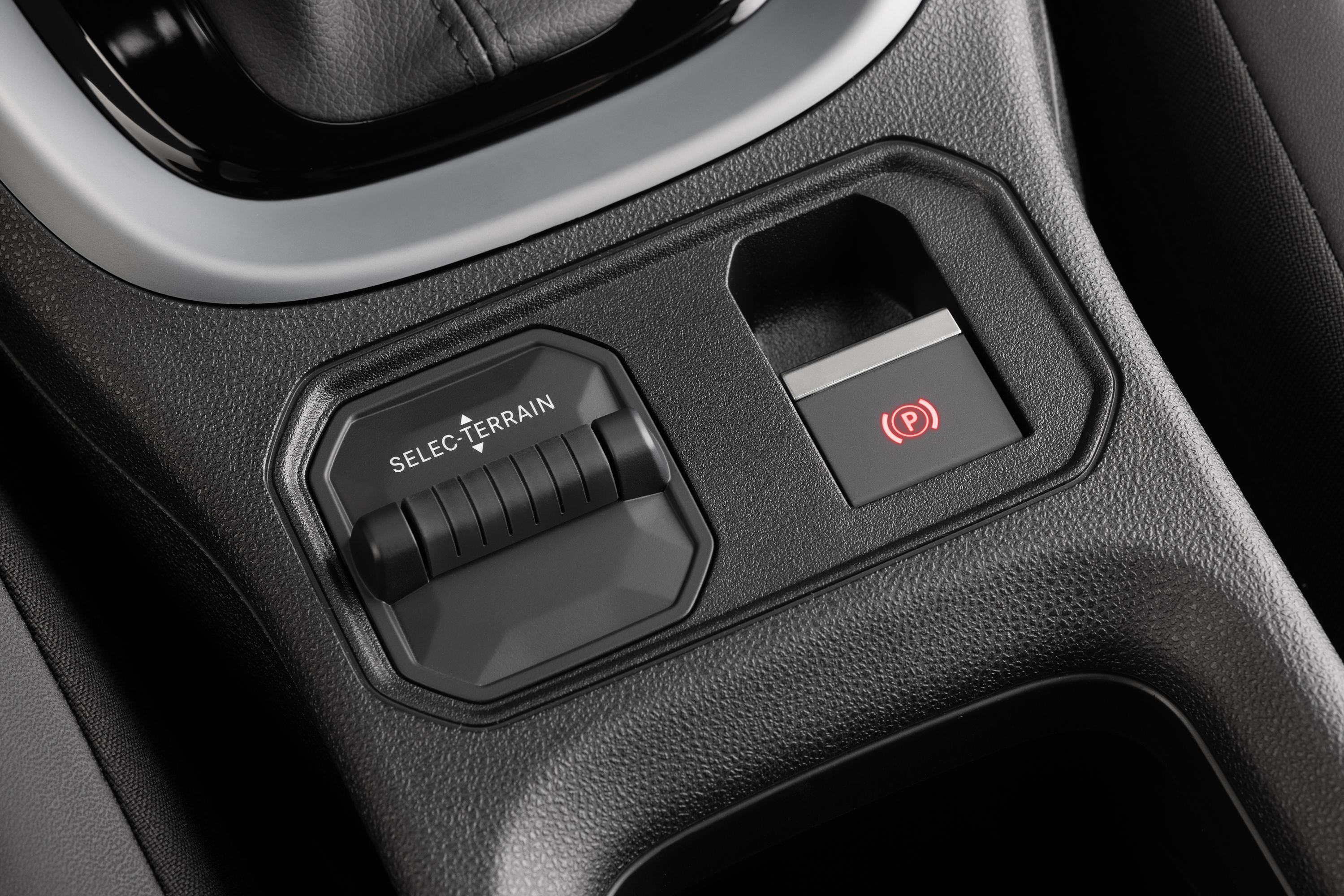 Detalhe do console central de um carro, mostrando o seletor de terreno SELEC-TERRAIN e o bot&atilde;o do freio de estacionamento eletr&ocirc;nico aceso em vermelho