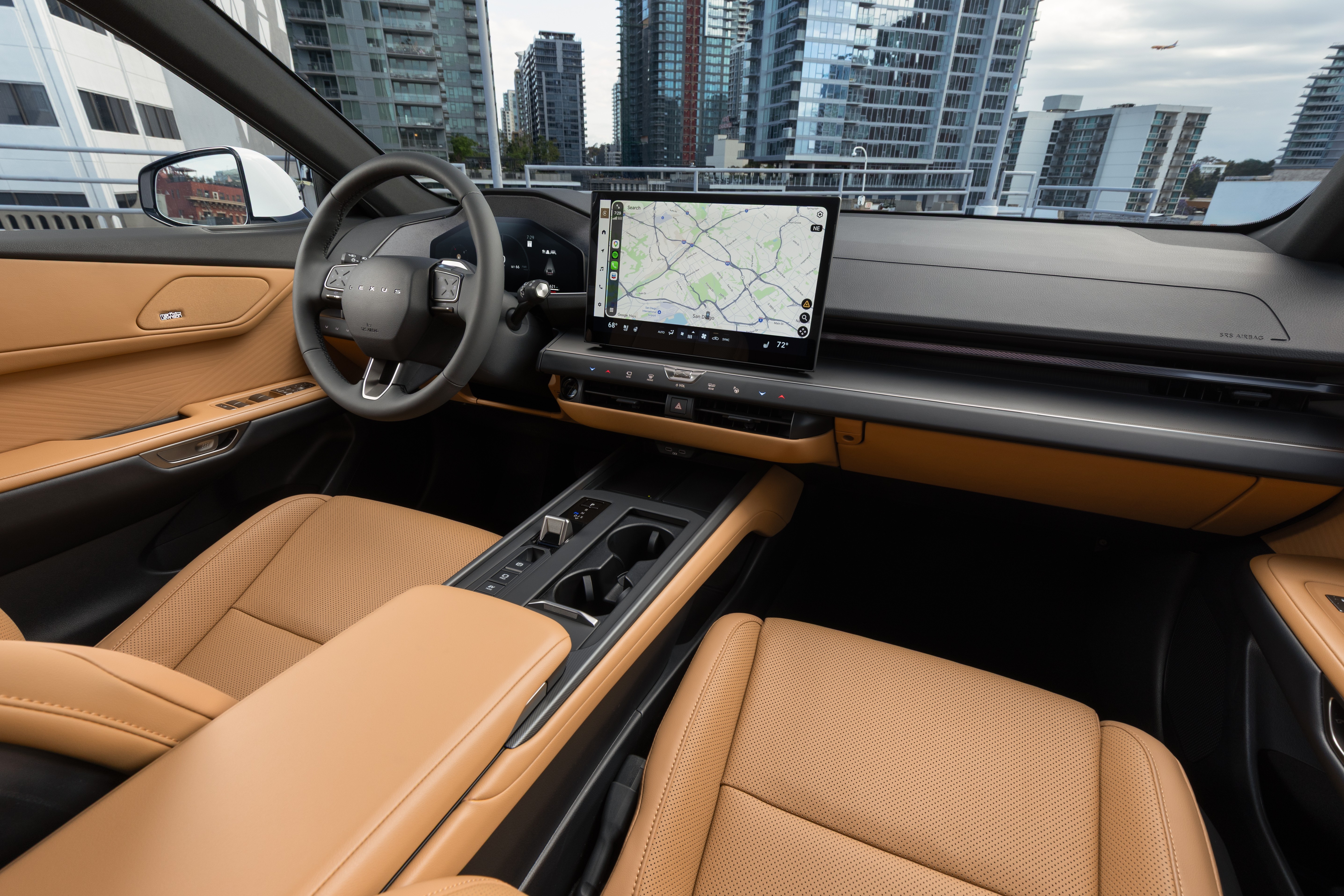 Interior de um carro moderno com bancos de couro marrom-claro e detalhes pretos. O painel possui uma tela grande exibindo um mapa de navega&ccedil;&atilde;o. Ao fundo, pr&eacute;dios altos e um c&eacute;u nublado com um avi&atilde;o distante