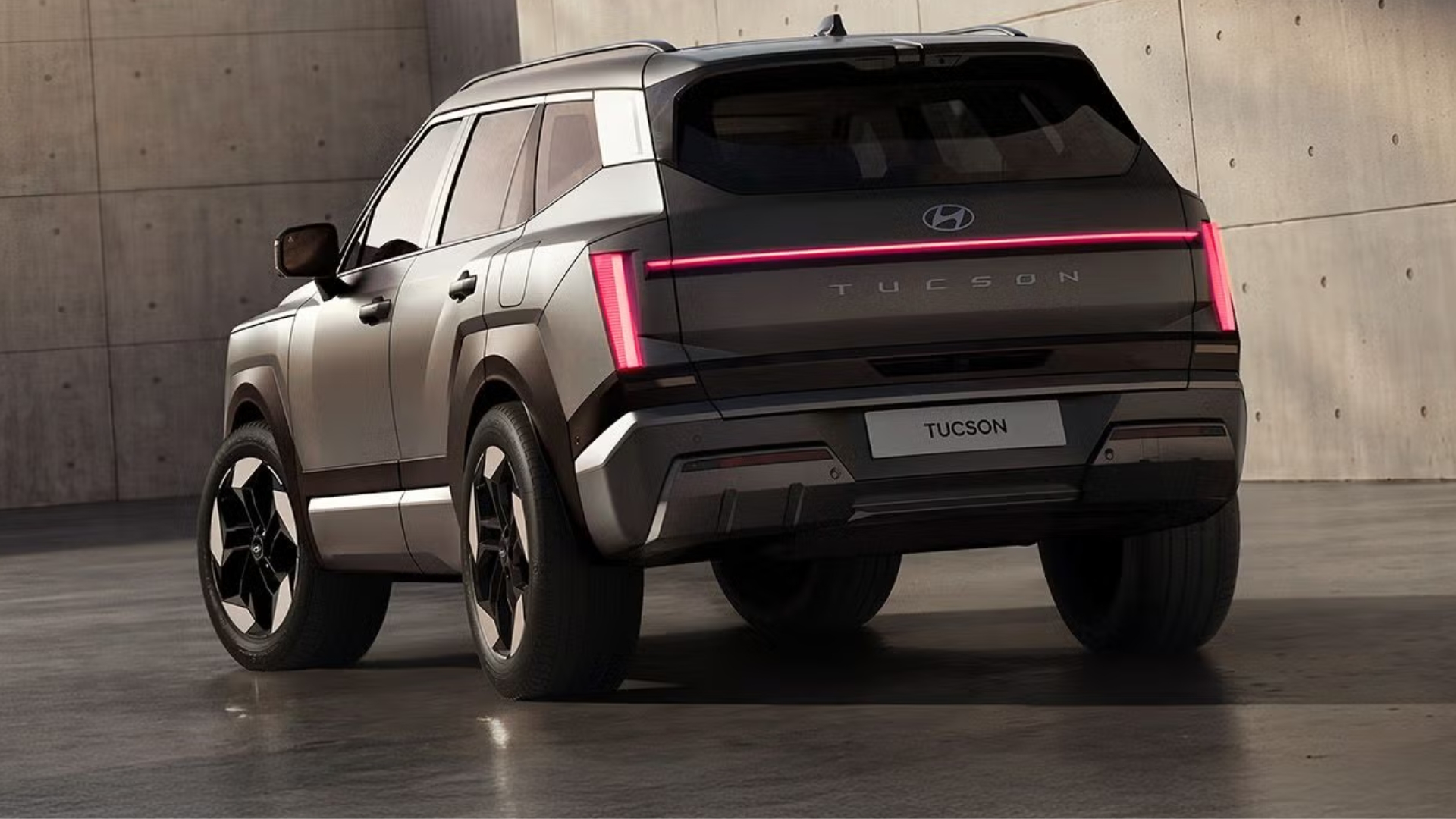 SUV Hyundai Tucson cinza escuro visto por tr&aacute;s, com lanternas traseiras em LED vermelhas acesas e uma linha horizontal luminosa. O carro est&aacute; estacionado em um piso de concreto polido, com uma parede de concreto ao fundo