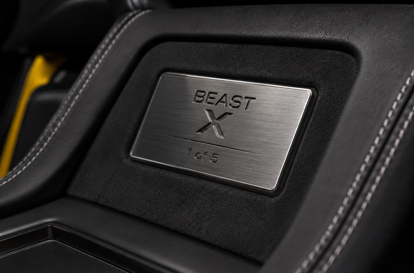 Placa met&aacute;lica escovada com a inscri&ccedil;&atilde;o BEAST X 1 of 5 em relevo, embutida no console central de um carro, cercada por estofamento preto com costura branca