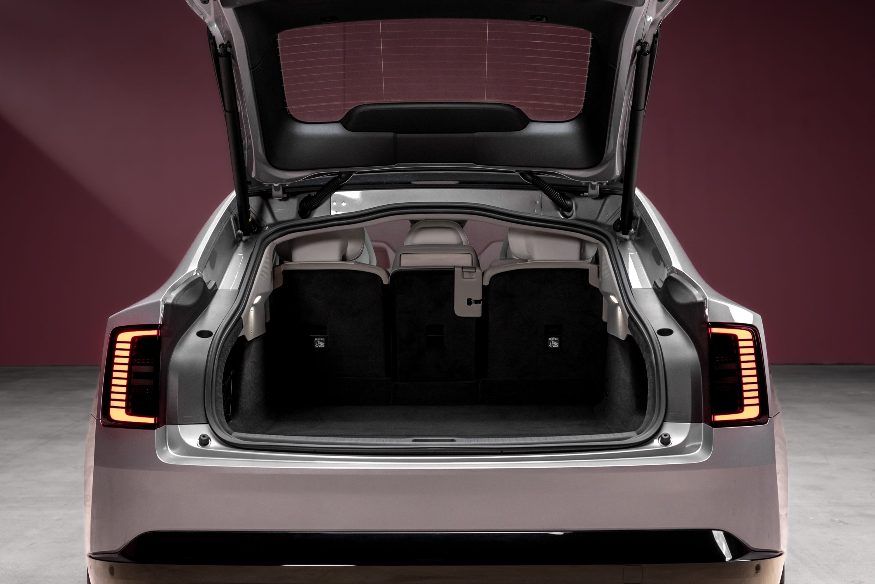 Traseira de um carro cinza com a tampa do porta-malas aberta, revelando o interior espa&ccedil;oso e os bancos traseiros rebatidos. As lanternas traseiras, com design vertical de LEDs, est&atilde;o acesas