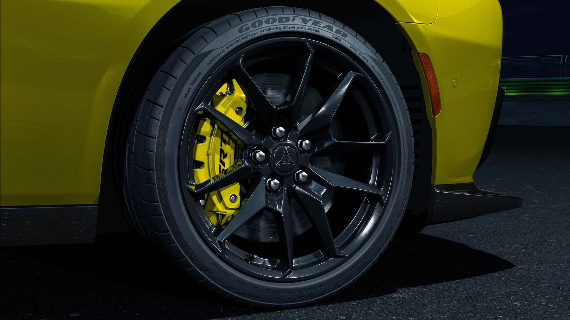 Roda preta de liga leve com m&uacute;ltiplos raios e pneu Goodyear, freio a disco amarelo brilhante, parte da lateral amarela de um carro esportivo