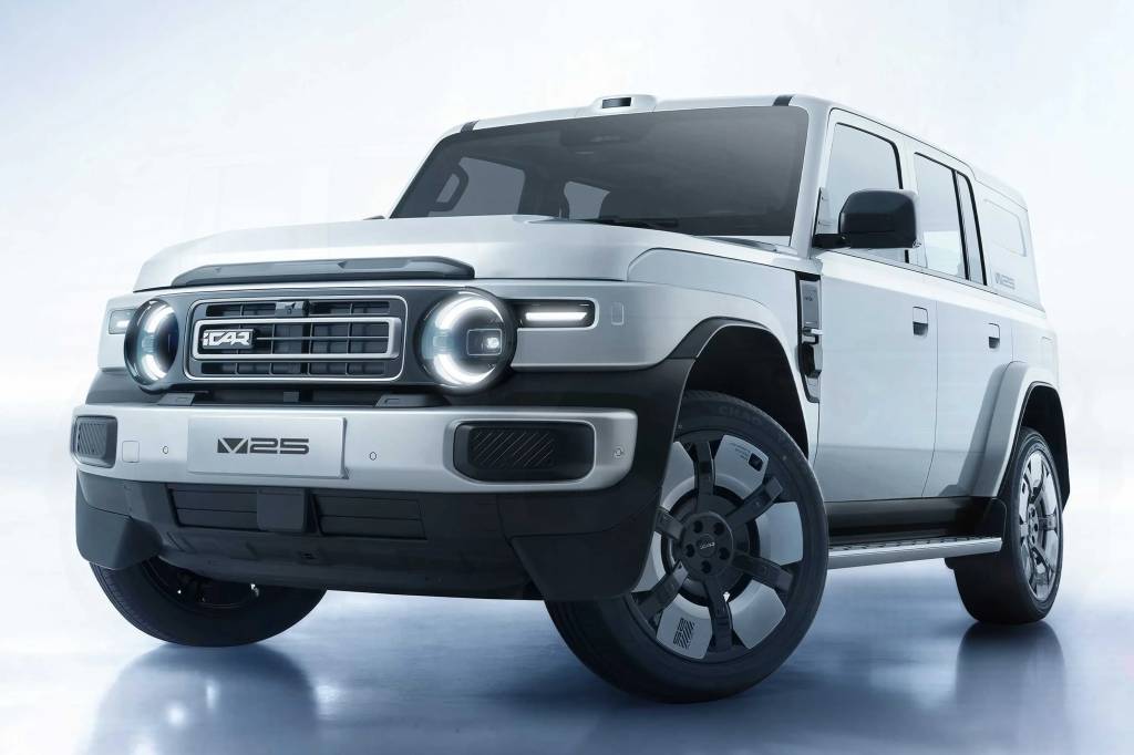 SUV el&eacute;trico iCAR V23 prateado, com design robusto e moderno, far&oacute;is redondos acesos e grade frontal com o logo iCAR, exibido em um est&uacute;dio com fundo claro e reflexo no ch&atilde;o