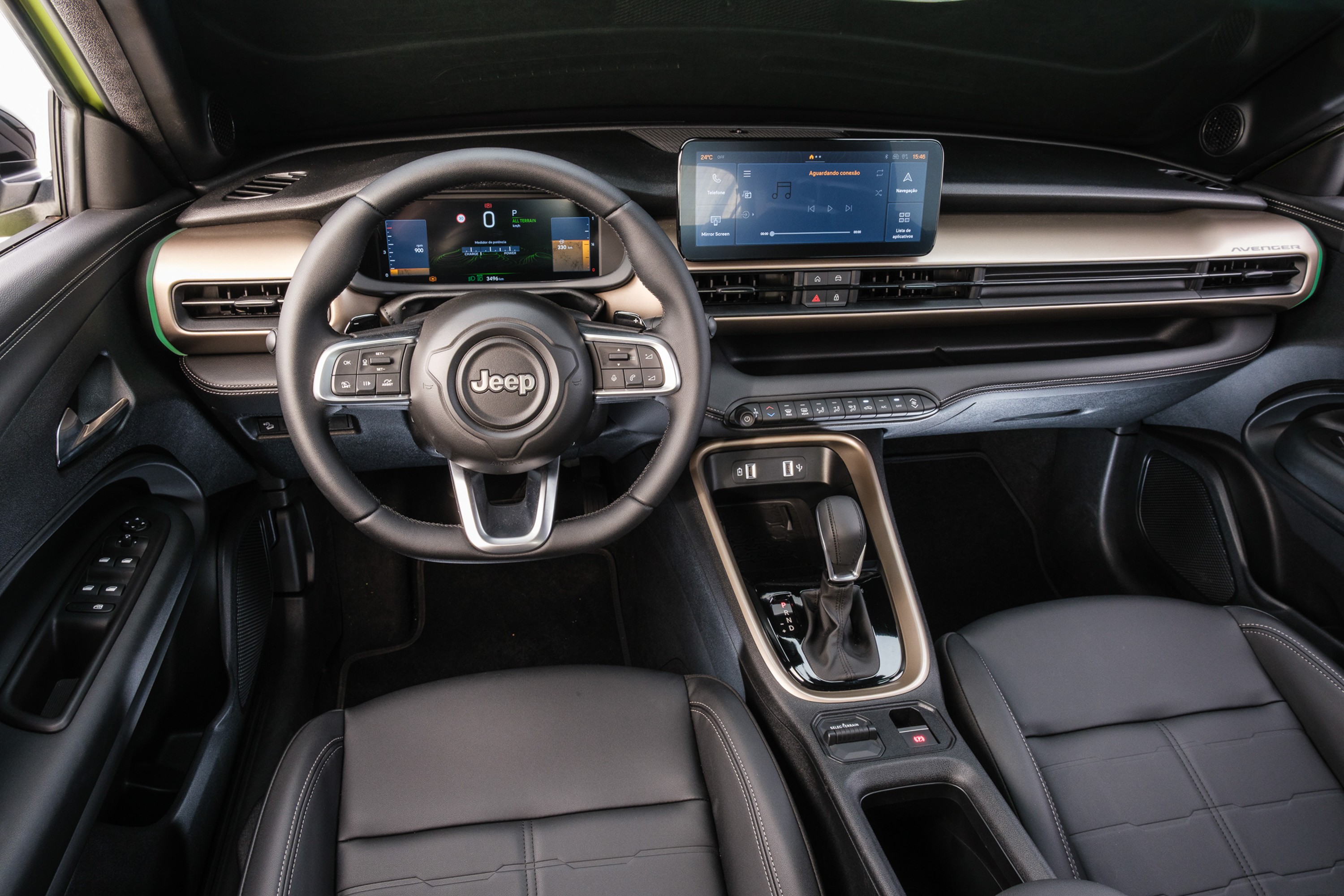 Interior de um carro Jeep moderno, com volante preto e logo Jeep central. O painel possui duas telas digitais, uma para o veloc&iacute;metro e outra multim&iacute;dia. Detalhes em bronze e preto no painel e console central, com bancos de couro pretos. A alavanca de c&acirc;mbio &eacute; preta e compacta. A porta do motorista tem bot&otilde;es para vidros e travas.