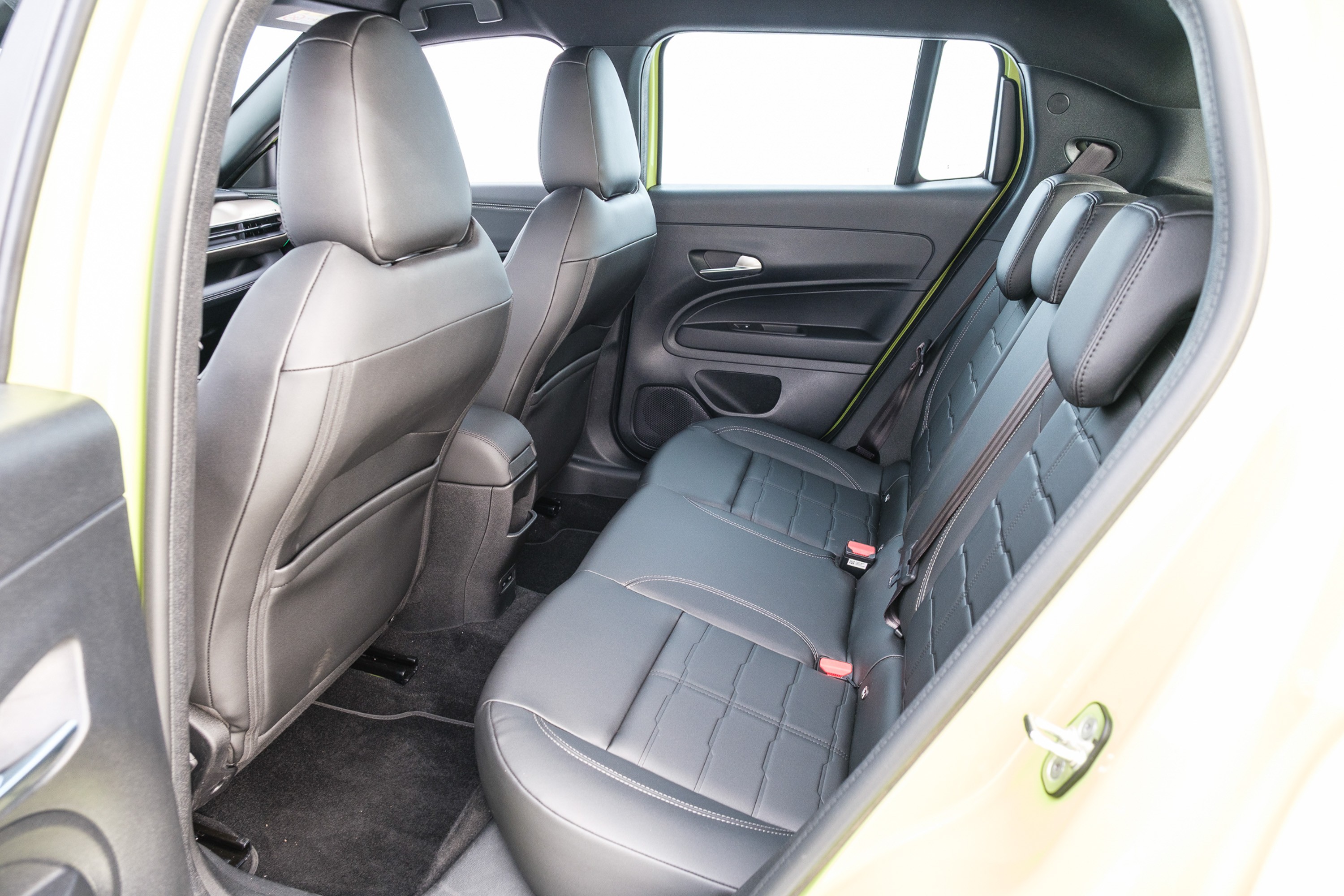 Interior de um carro com bancos de couro preto, mostrando os assentos traseiros e a parte de tr&aacute;s dos bancos dianteiros. As janelas est&atilde;o claras, e o acabamento interno tem detalhes em verde-lim&atilde;o