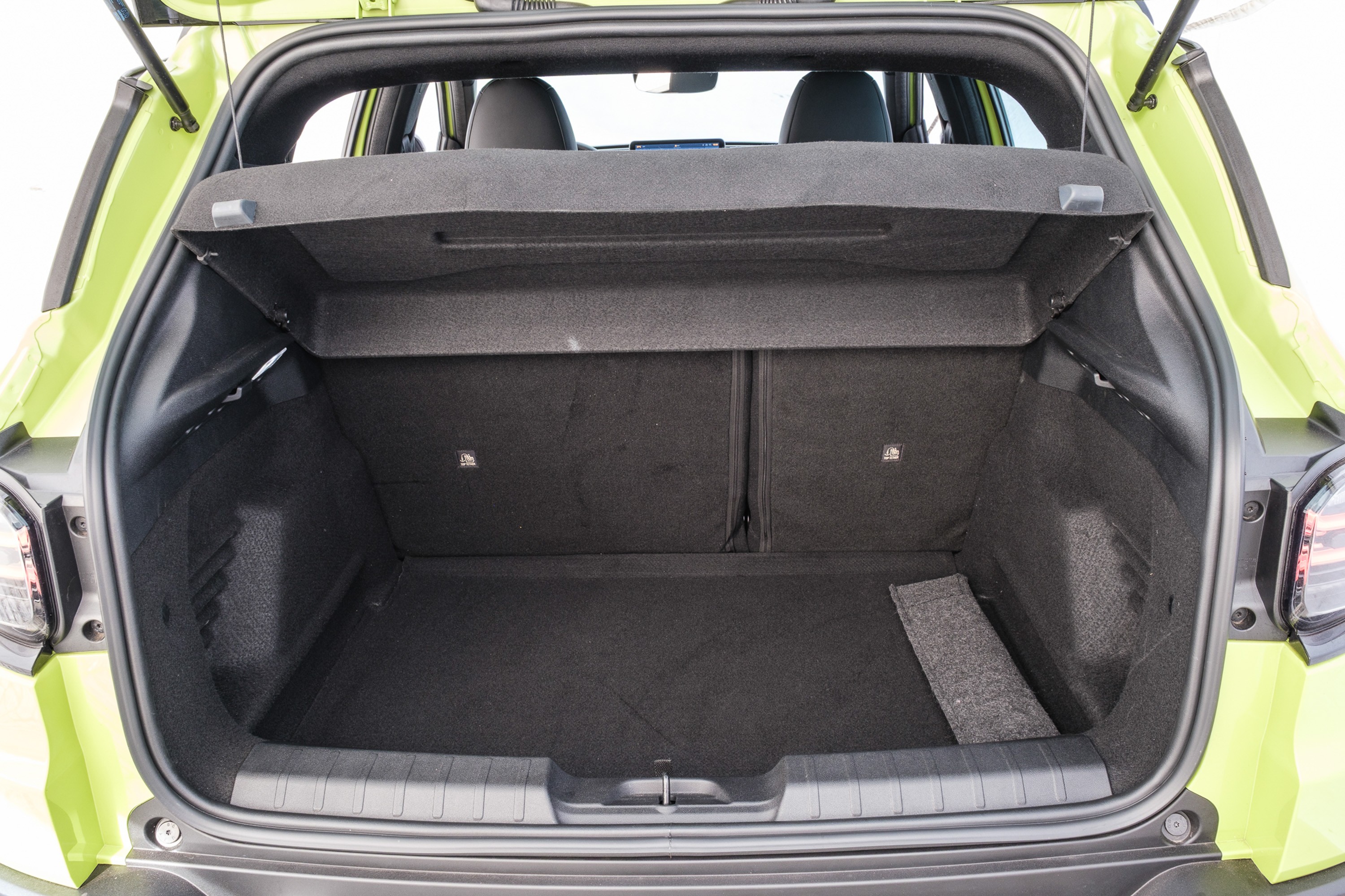 Porta-malas de um carro verde-lim&atilde;o aberto, mostrando o interior forrado em carpete preto, com o tamp&atilde;o do porta-malas levantado e os bancos traseiros vis&iacute;veis ao fundo