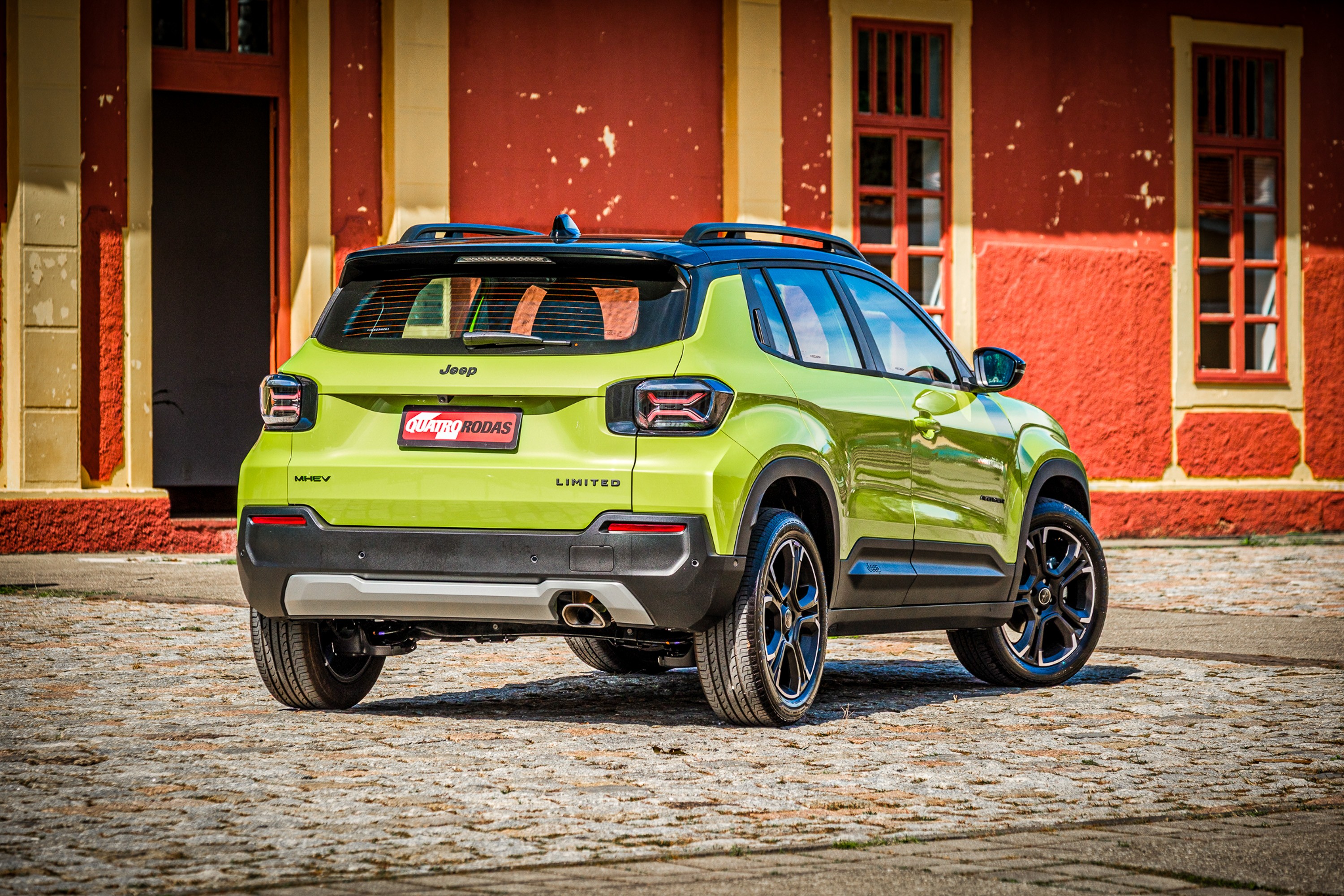SUV Jeep Renegade verde-lim&atilde;o, modelo Limited, estacionado de costas em rua de paralelep&iacute;pedos, com pr&eacute;dio vermelho e janelas de madeira ao fundo