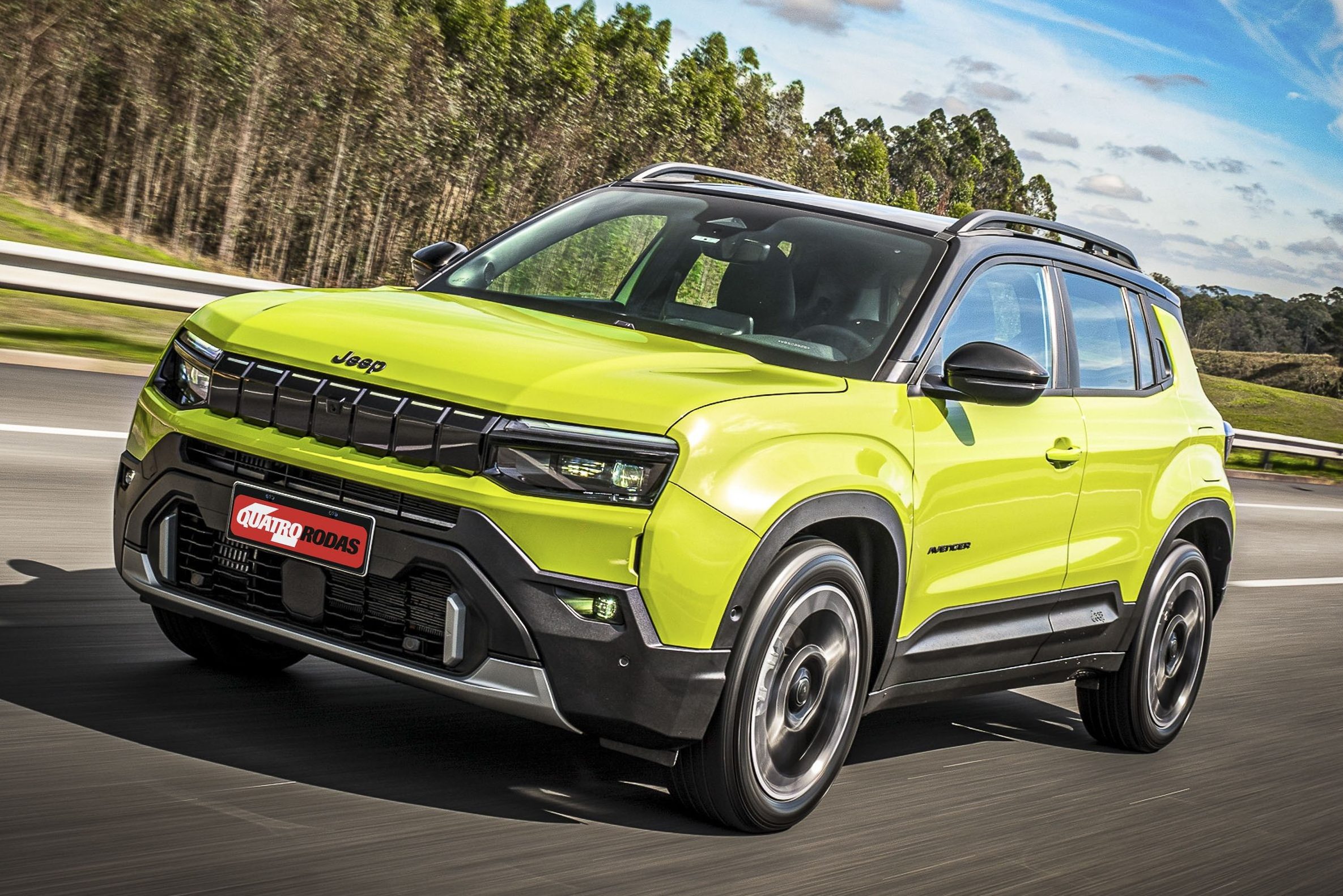 SUV Jeep Avenger amarelo-limão com teto preto, rodando em uma estrada asfaltada com árvores ao fundo e céu azul com nuvens esparsas