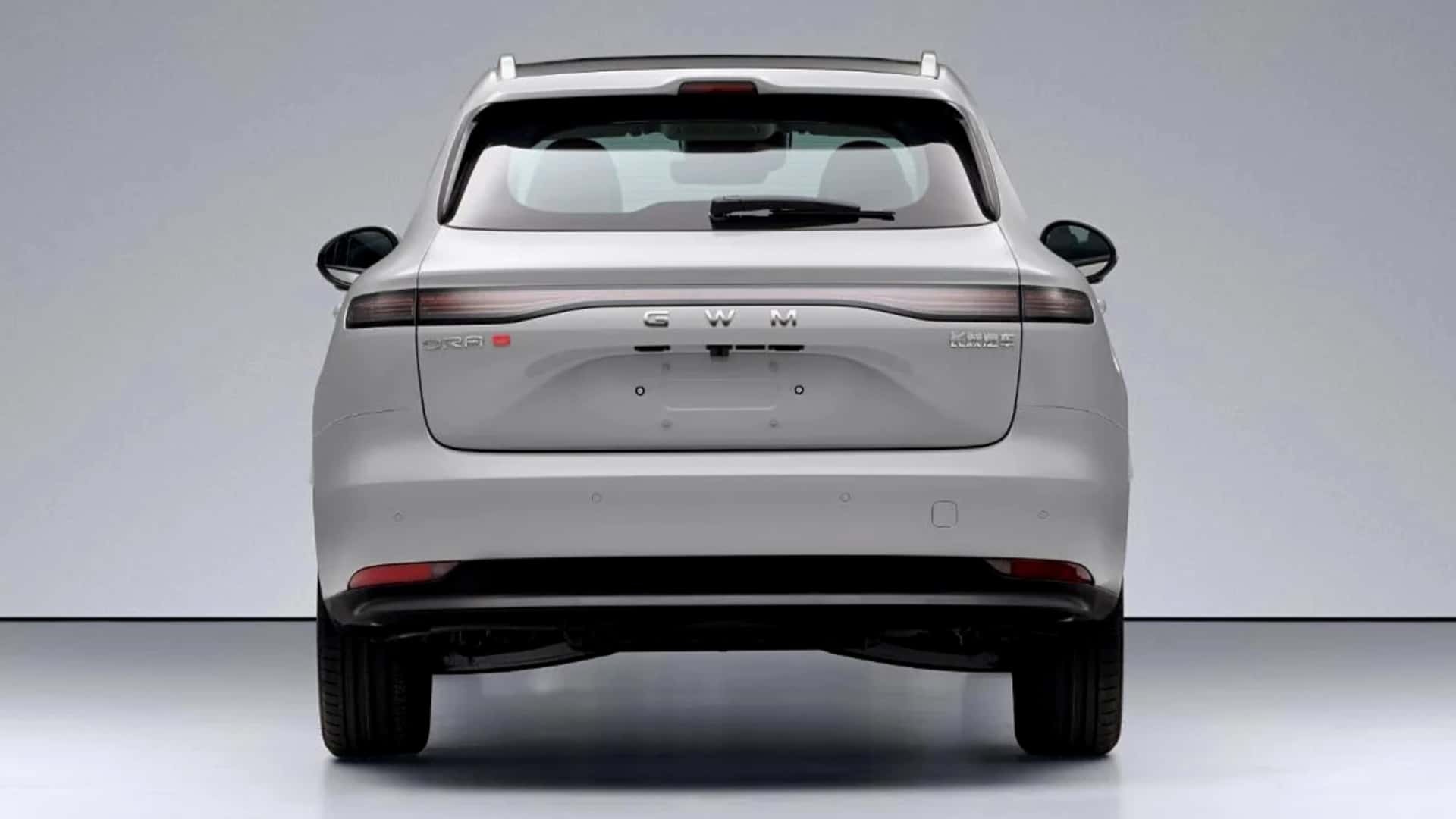 Traseira de um SUV branco com o logo GWM no centro da tampa do porta-malas. As lanternas horizontais se estendem pela largura do ve&iacute;culo, e h&aacute; um pequeno spoiler no teto. O para-choque traseiro &eacute; liso, com refletores vermelhos nas extremidades inferiores e dois escapamentos pretos vis&iacute;veis abaixo. O carro est&aacute; em um est&uacute;dio com fundo cinza claro