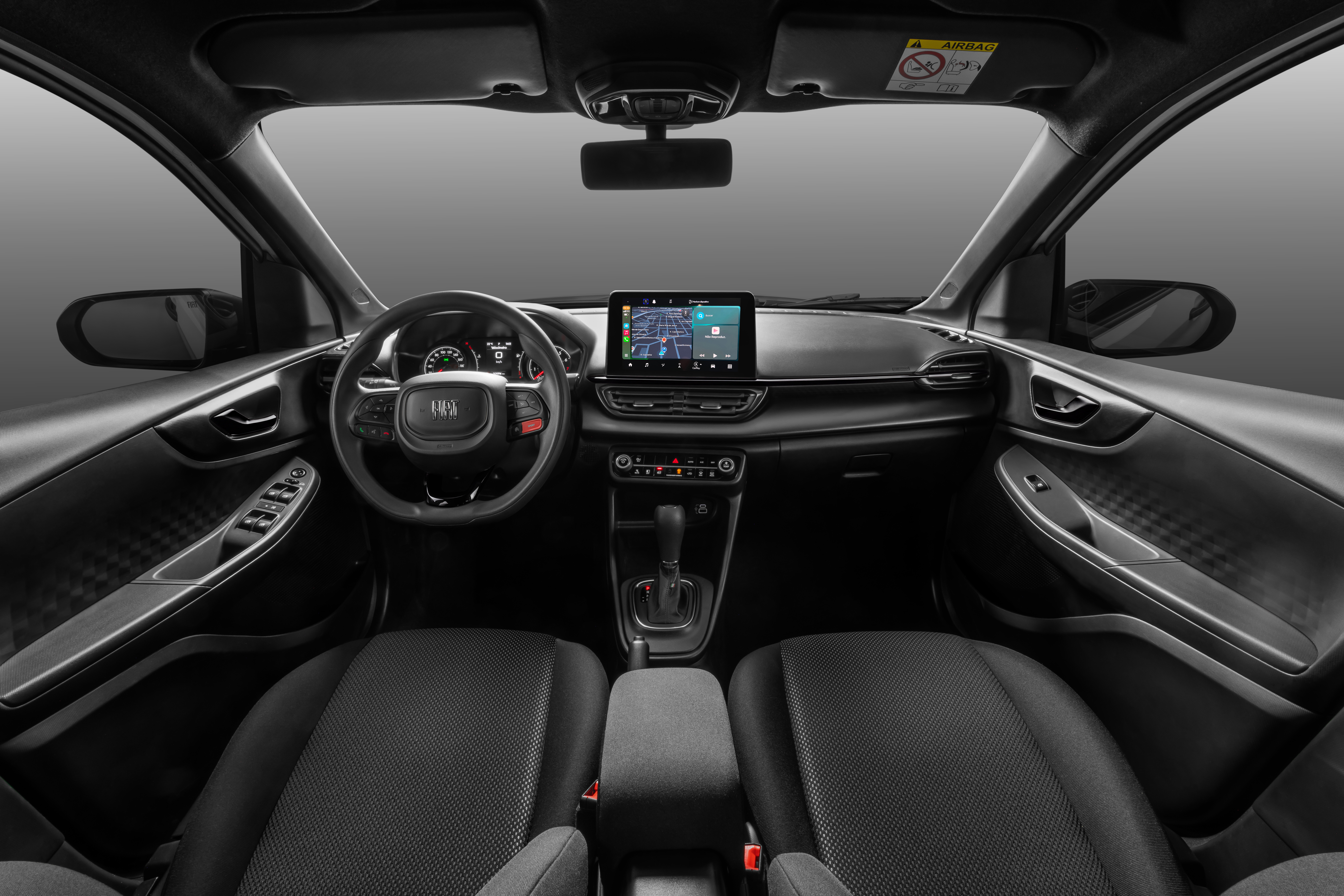 Interior de um carro moderno, com bancos pretos de tecido, volante multifuncional e painel escuro. Uma tela multim&iacute;dia central exibe um mapa de navega&ccedil;&atilde;o.