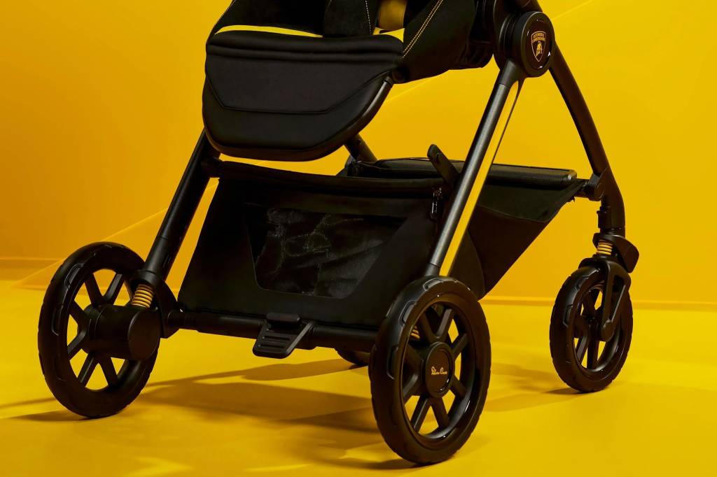 Carrinho de beb&ecirc; preto com detalhes amarelos, estrutura met&aacute;lica e rodas pretas, em um fundo amarelo vibrante