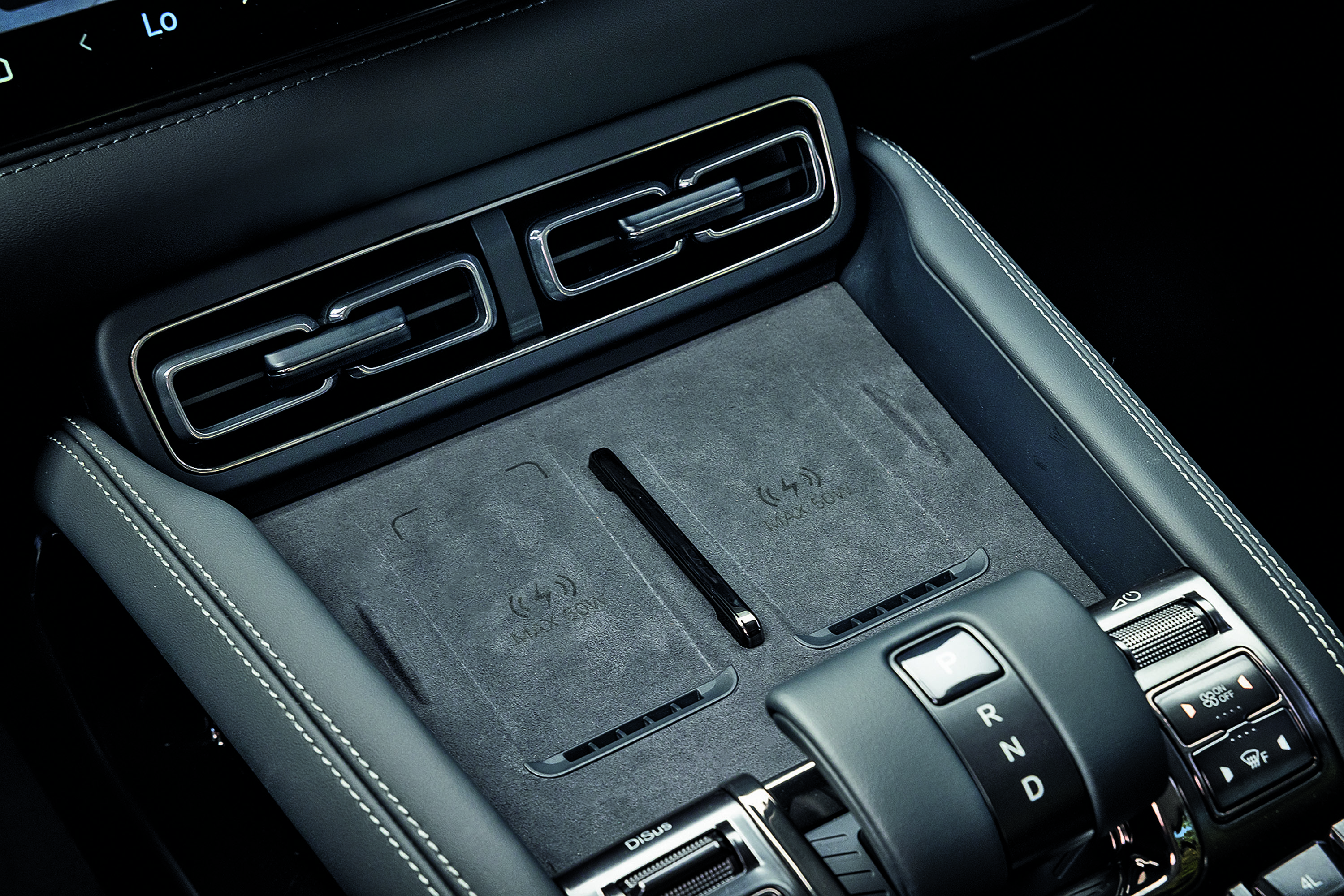 Interior de carro moderno com console central em couro preto e costura branca, dois carregadores de celular por indu&ccedil;&atilde;o, sa&iacute;das de ar cromadas e alavanca de c&acirc;mbio autom&aacute;tica